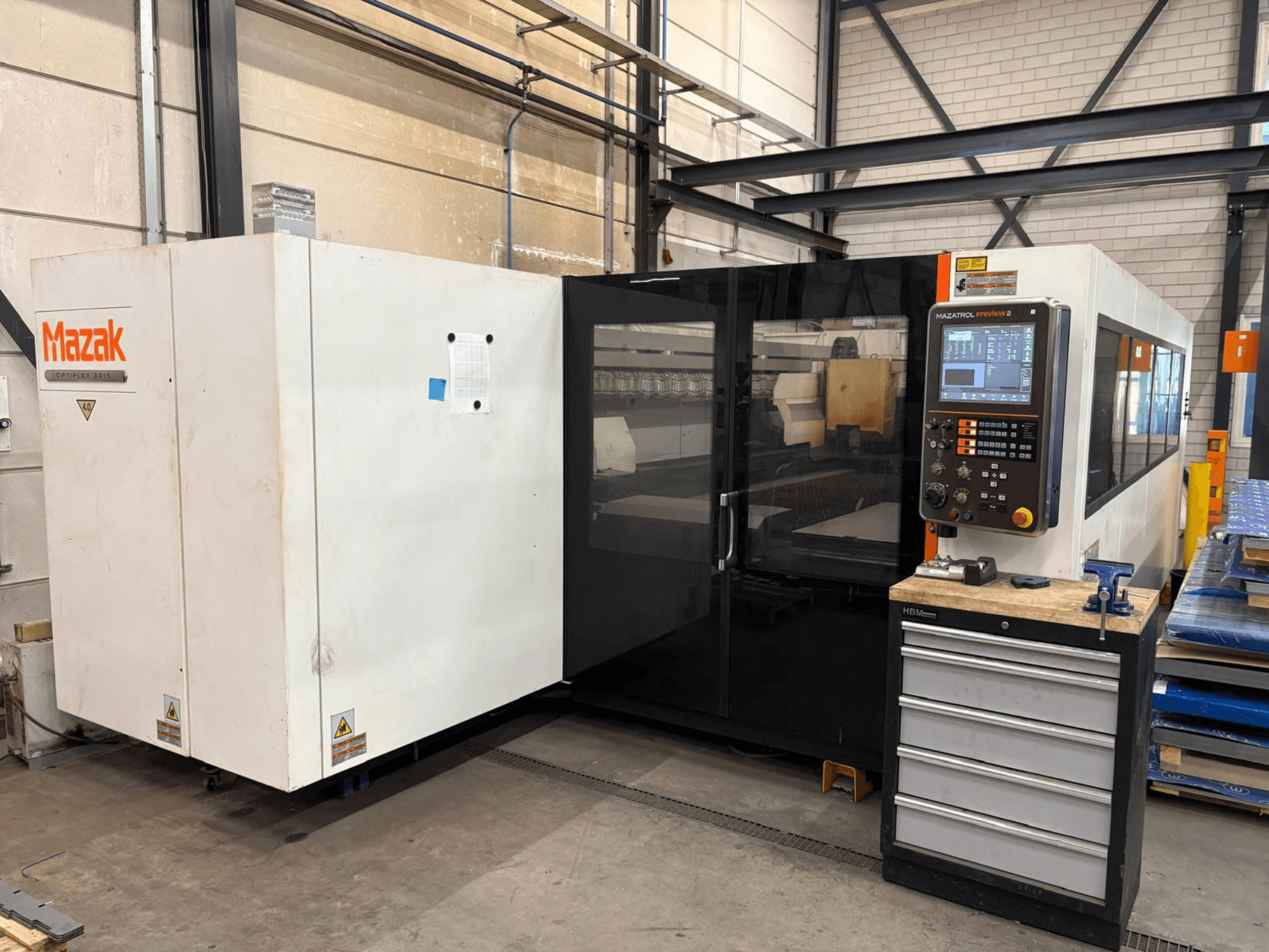 Mazak Optiplex 3015 CO₂-Laserschneidmaschine, Vorderansicht, mit Bedienfeld und industrieller Umgebung.