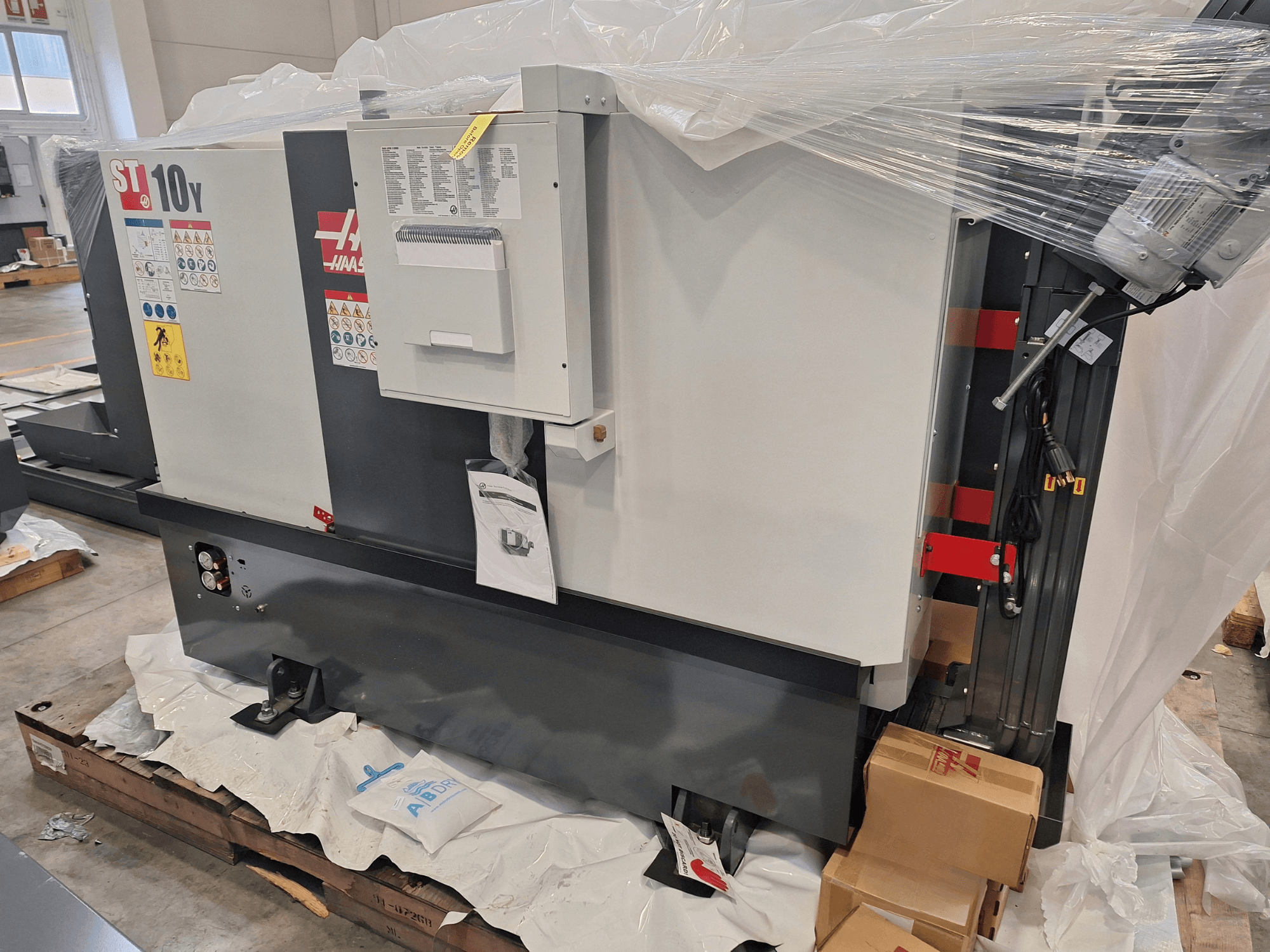 HAAS ST-10Y EU Horizontal-Drehmaschine, Seitenansicht, in Plastikfolie verpackt, mit sichtbarem Bedienfeld und Warnaufklebern.