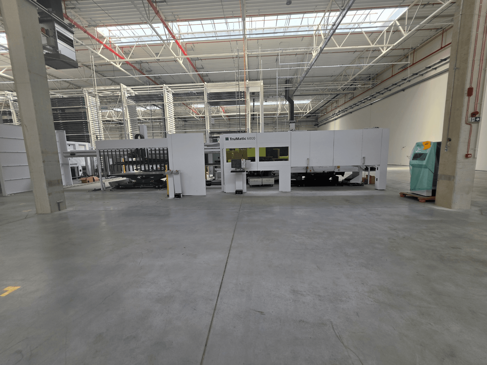 TRUMPF TruMatic 6000-1600 Faser-Stanz-Laser-Kombimaschine in einer großzügigen Lagerhalle, von vorne gesehen.