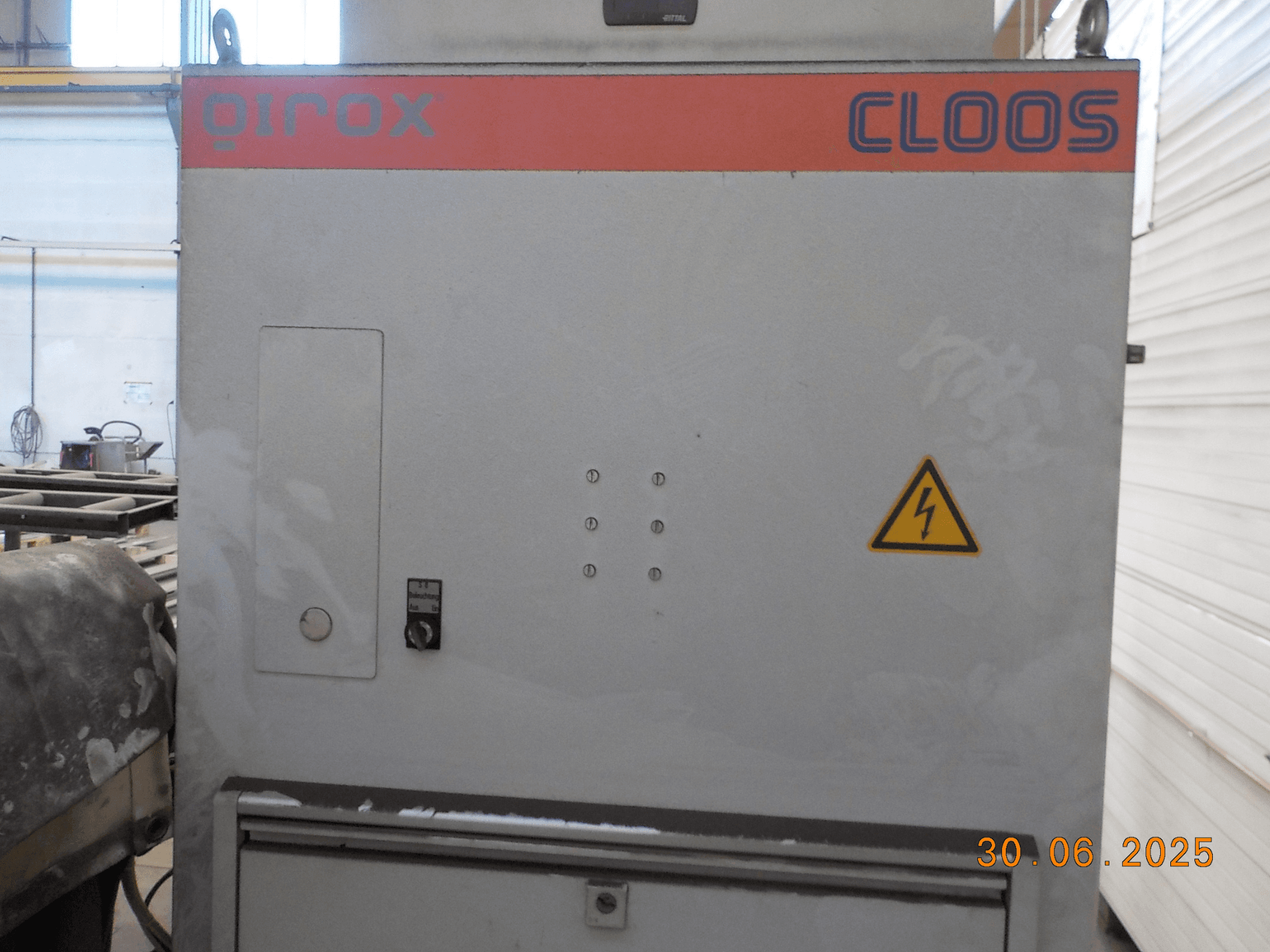 Seitenansicht der Schweißmaschine Cloos QIROX mit Bedienfeld und Warnschild, mit staubiger Oberfläche und sichtbarem Datumsstempel.