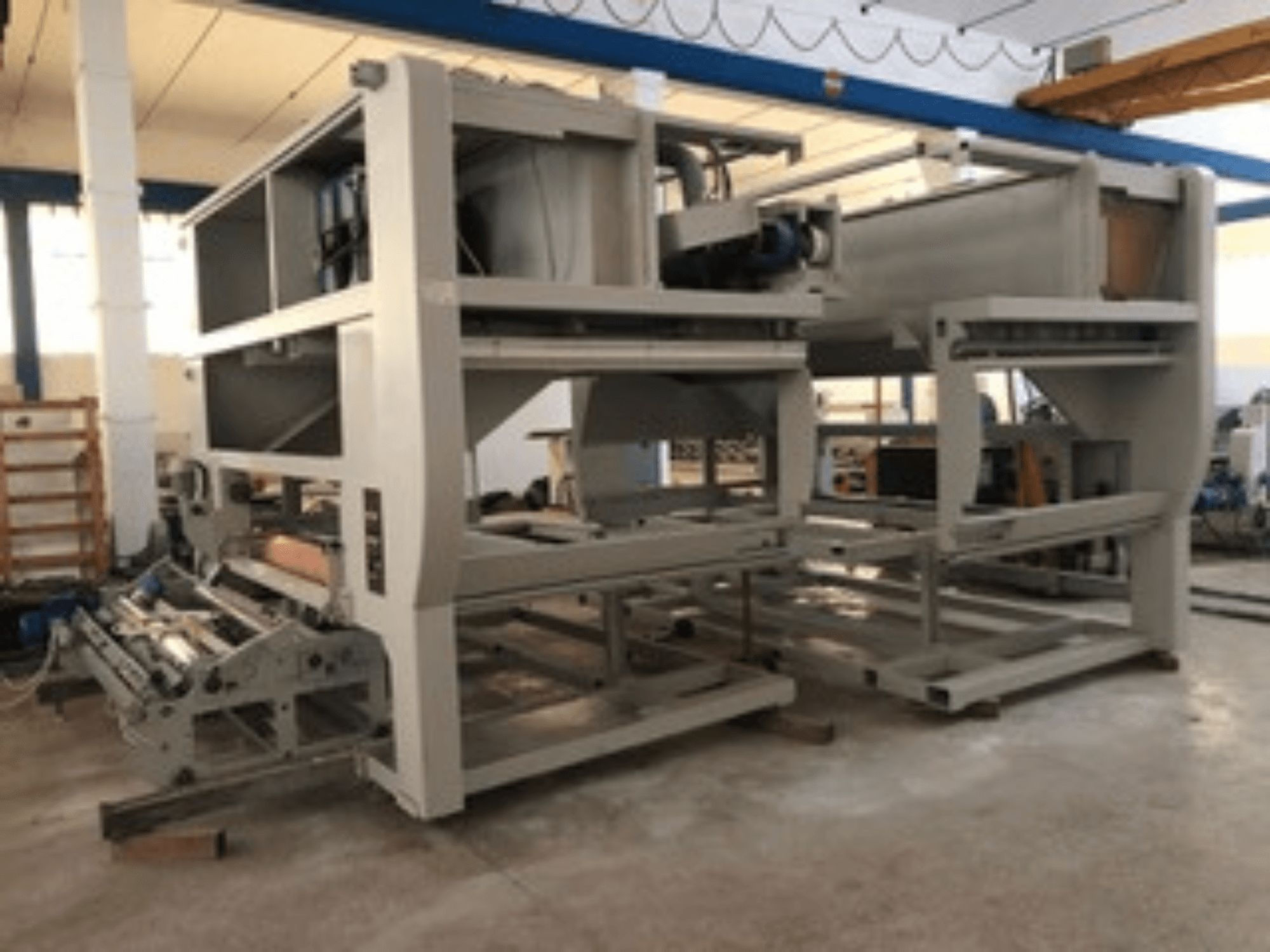 Industriemaschine mit mehreren Förderrollen und großer Struktur; Seitenansicht, graue Farbe, in einer gut beleuchteten Fabrik.