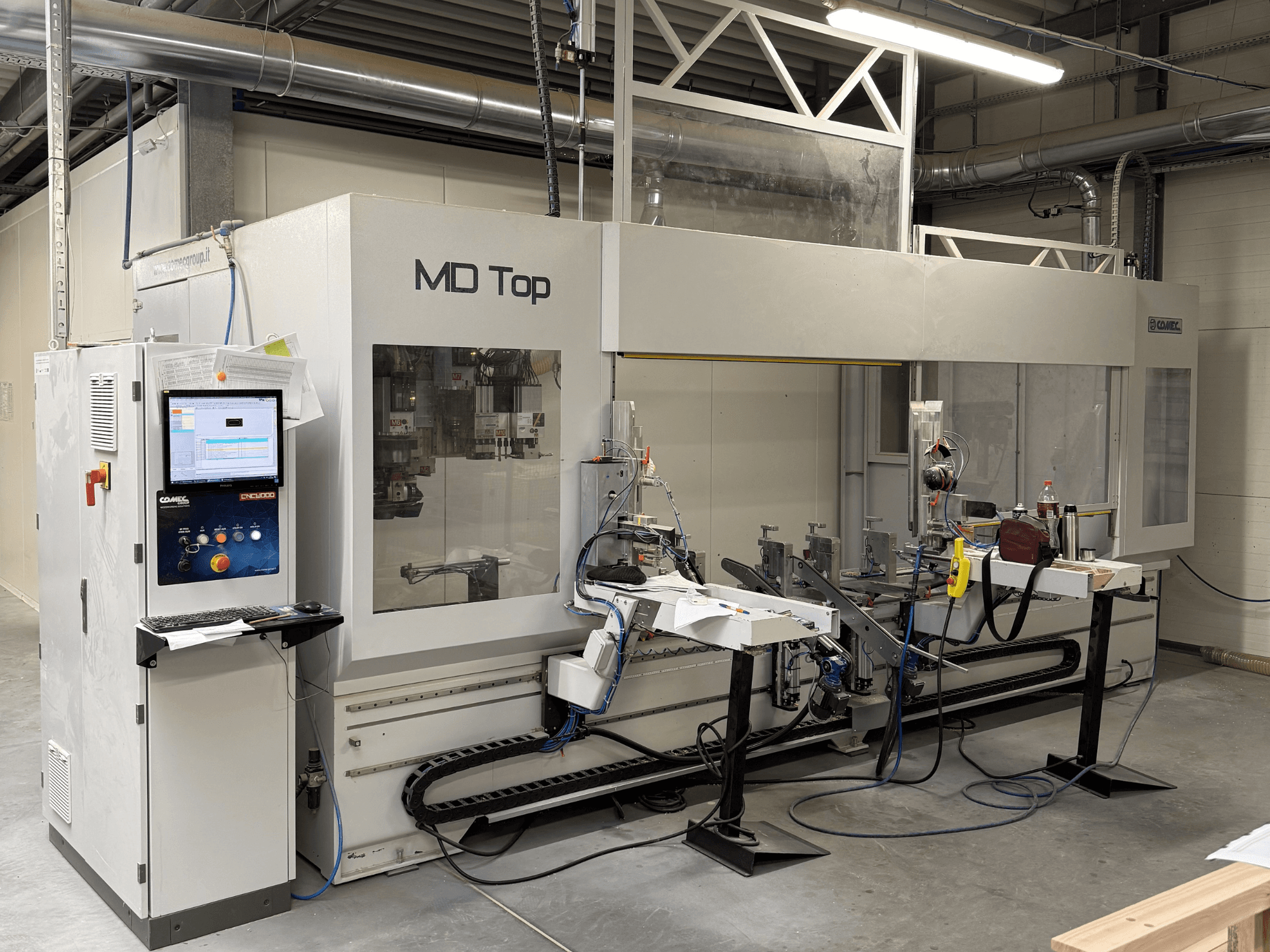 MD Top CNC-Maschine von vorne gesehen, mit Bedienfeld, Roboterarmen und Arbeitsbereich mit Werkzeugen und Materialien.