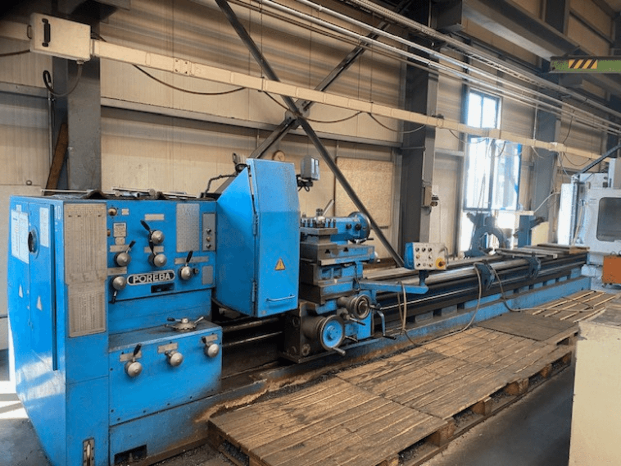 Vorderansicht einer blauen POREBA-Drehmaschine mit Bedienknöpfen, einer Werkzeugauflage und Holzpaletten darunter.