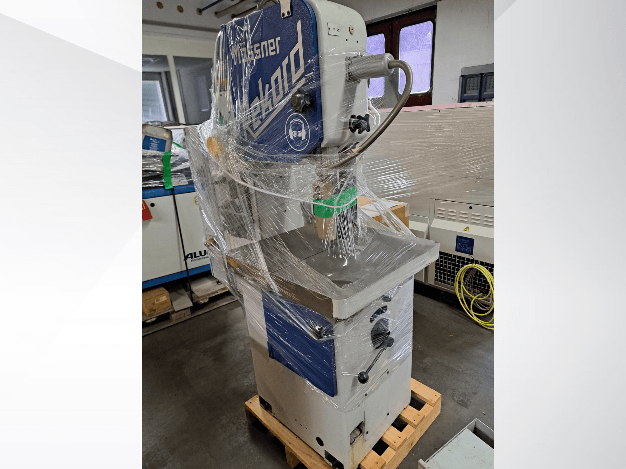 MOSSNER Rekord-Metallbandsäge, in Plastikfolie verpackt; Seitenansicht mit Bedienfeld und Sockel auf einer Holzpalette in einer Werkstatt.