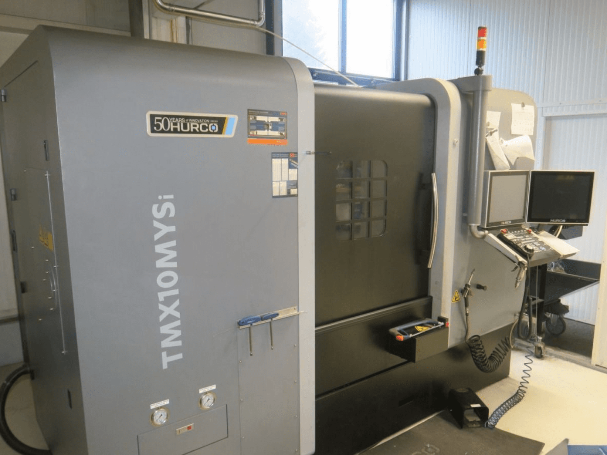 Hurco TMX10MYSi CNC-Maschine in der Seitenansicht; mit Bedienfeld, Notbeleuchtung und angezeigten Messinstrumenten.