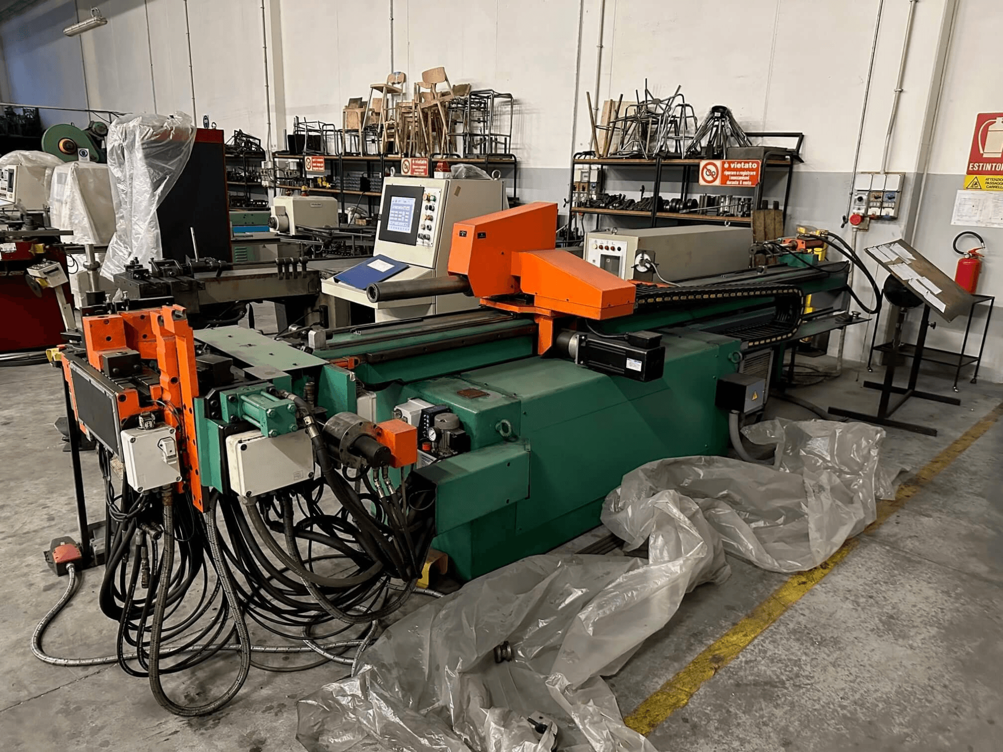 Industriemaschine mit orange-grünem Gehäuse, Schalttafel und zahlreichen Kabeln, von vorne gesehen in einer Werkstatt.