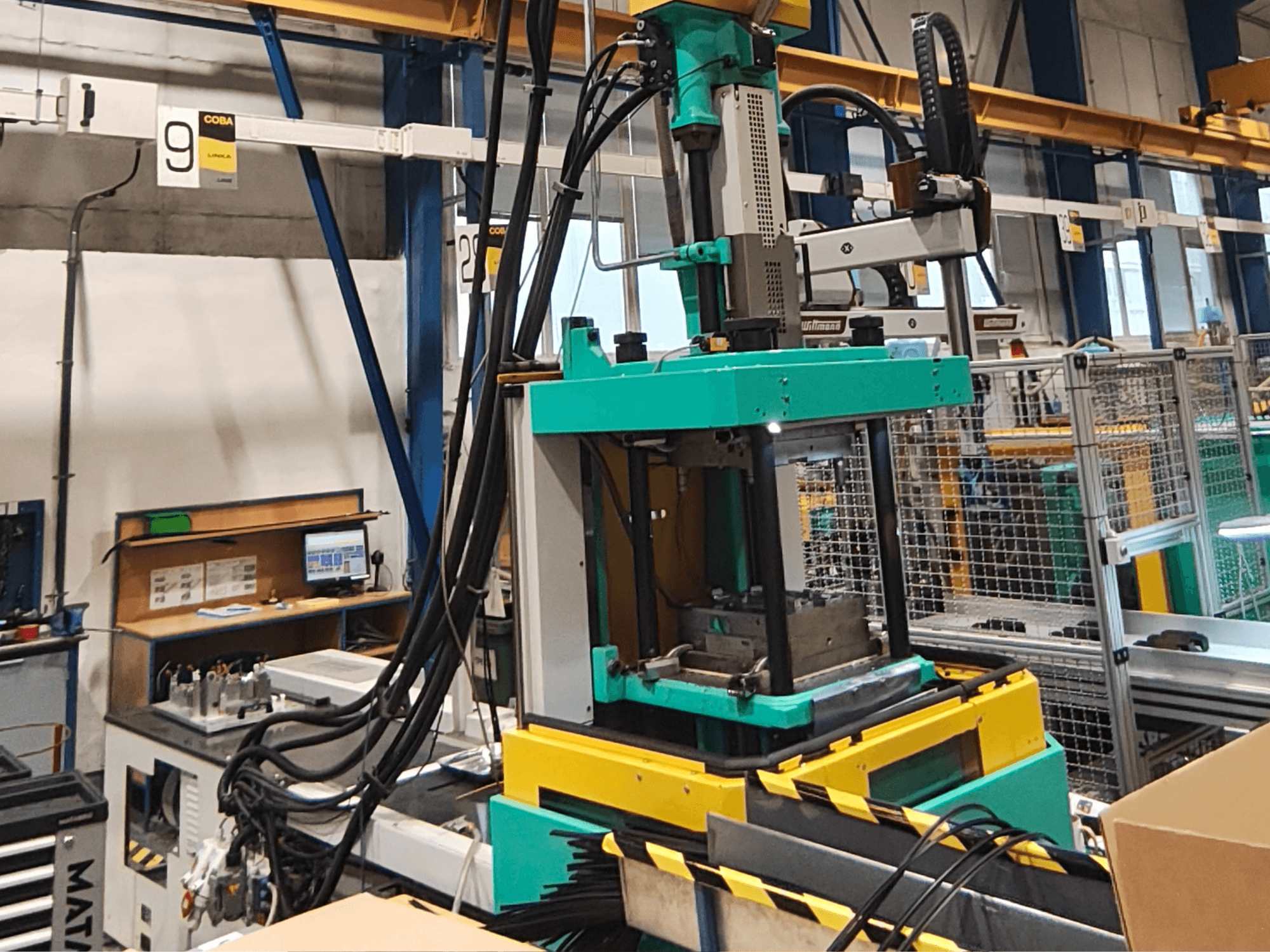 Grüne und gelbe hydraulische Pressmaschine in einer Fabrik, Vorderansicht, mit sichtbarem Bedienfeld und Kabeln an der Seite.