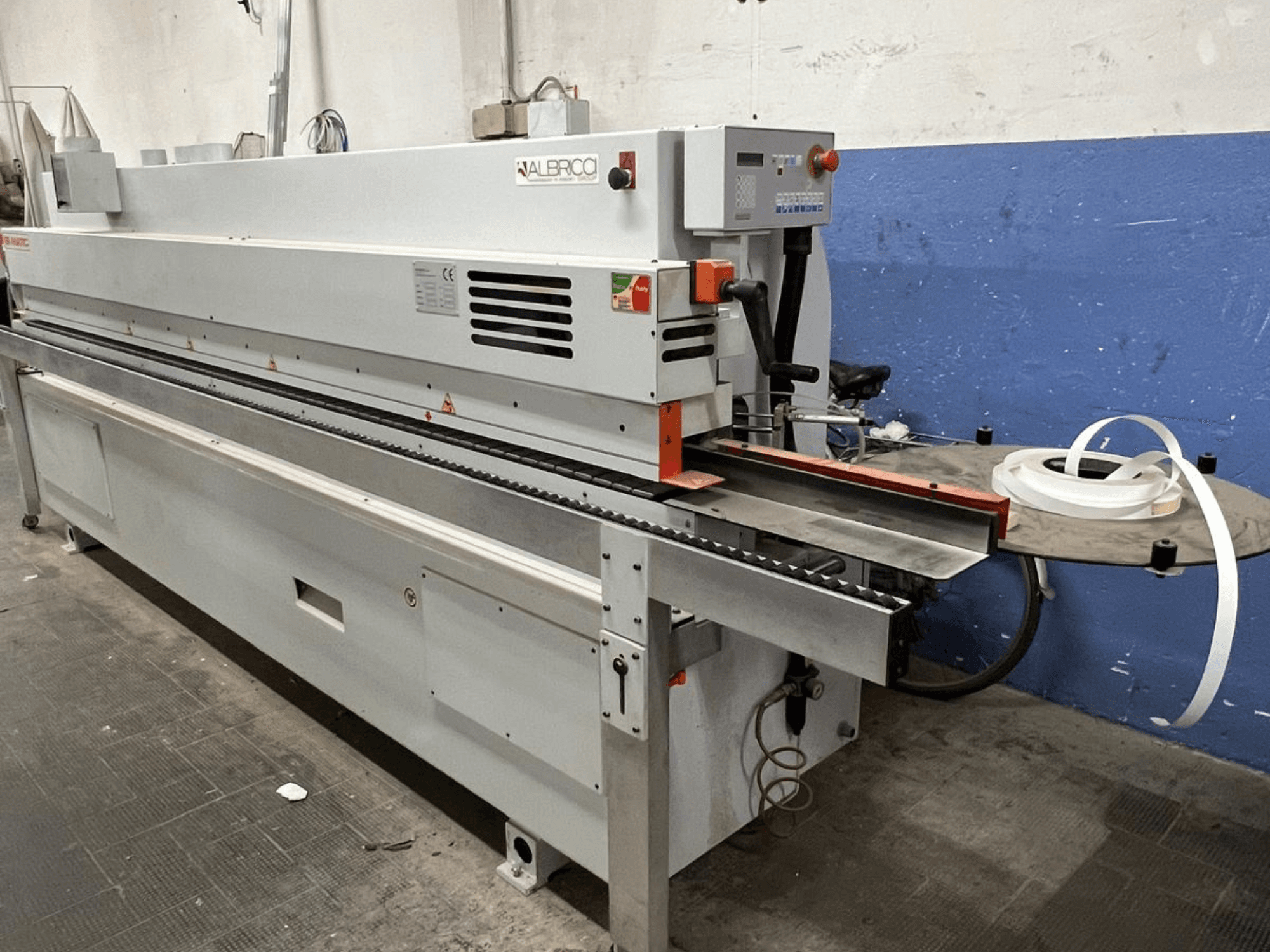 ALBRICO-Kantenanleimmaschine in der Frontansicht mit langem Transportband und einer angebrachten Klebebandrolle.