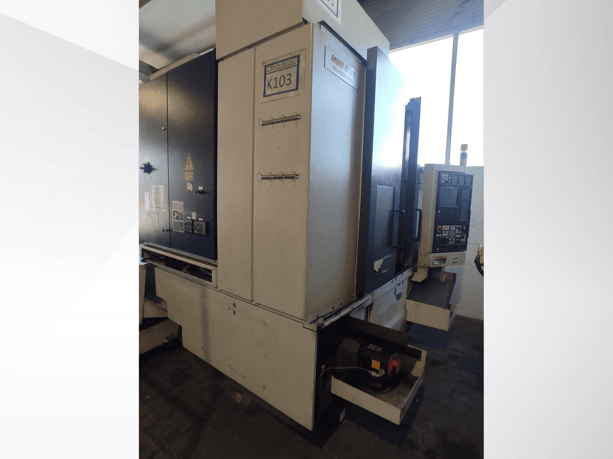 Mori Seiki K103 CNC-Maschine in der Vorderansicht, mit Bedienfeld, Sicherheitsschildern und sichtbaren elektrischen Komponenten.