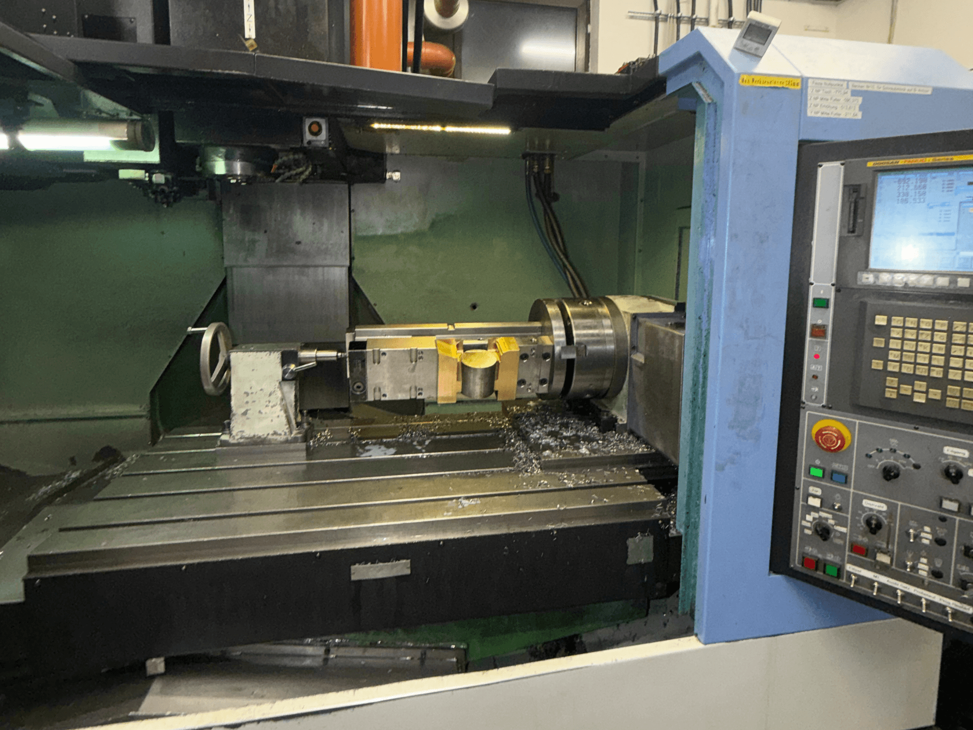 Vertikales Bearbeitungszentrum DOOSAN DNM650, Vorderansicht, mit dem Schneidwerkzeug und dem Bedienfeld im Vordergrund; auf dem Tisch sind Metallspäne zu sehen.