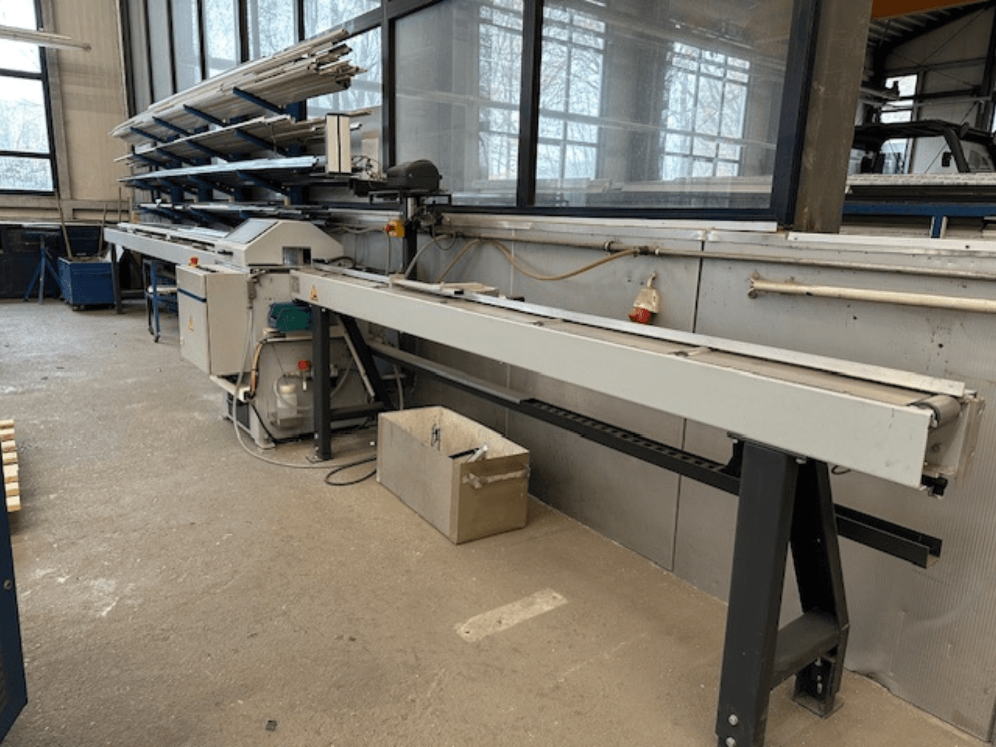 SCHÜCO PGS Metallkreissäge in einer Werkstatt, Seitenansicht mit verstellbarem Schneidbett und einem Regal mit Metallprofilen darüber.