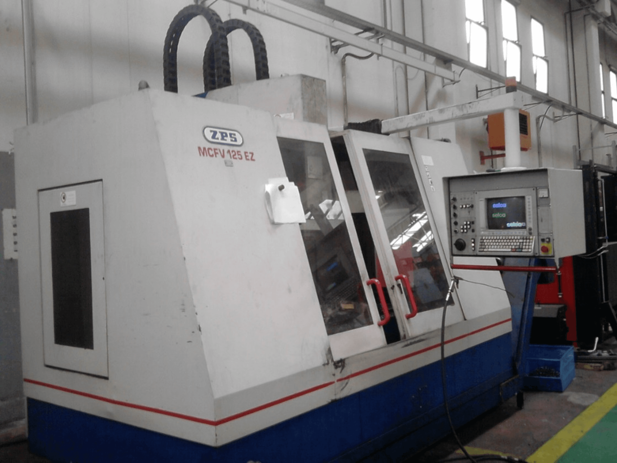 ZPS MCFV 125 EZ CNC-Maschine, Vorderansicht mit Bedienfeld und roten Griffen, in einer Werkstattumgebung mit sichtbaren Schläuchen.