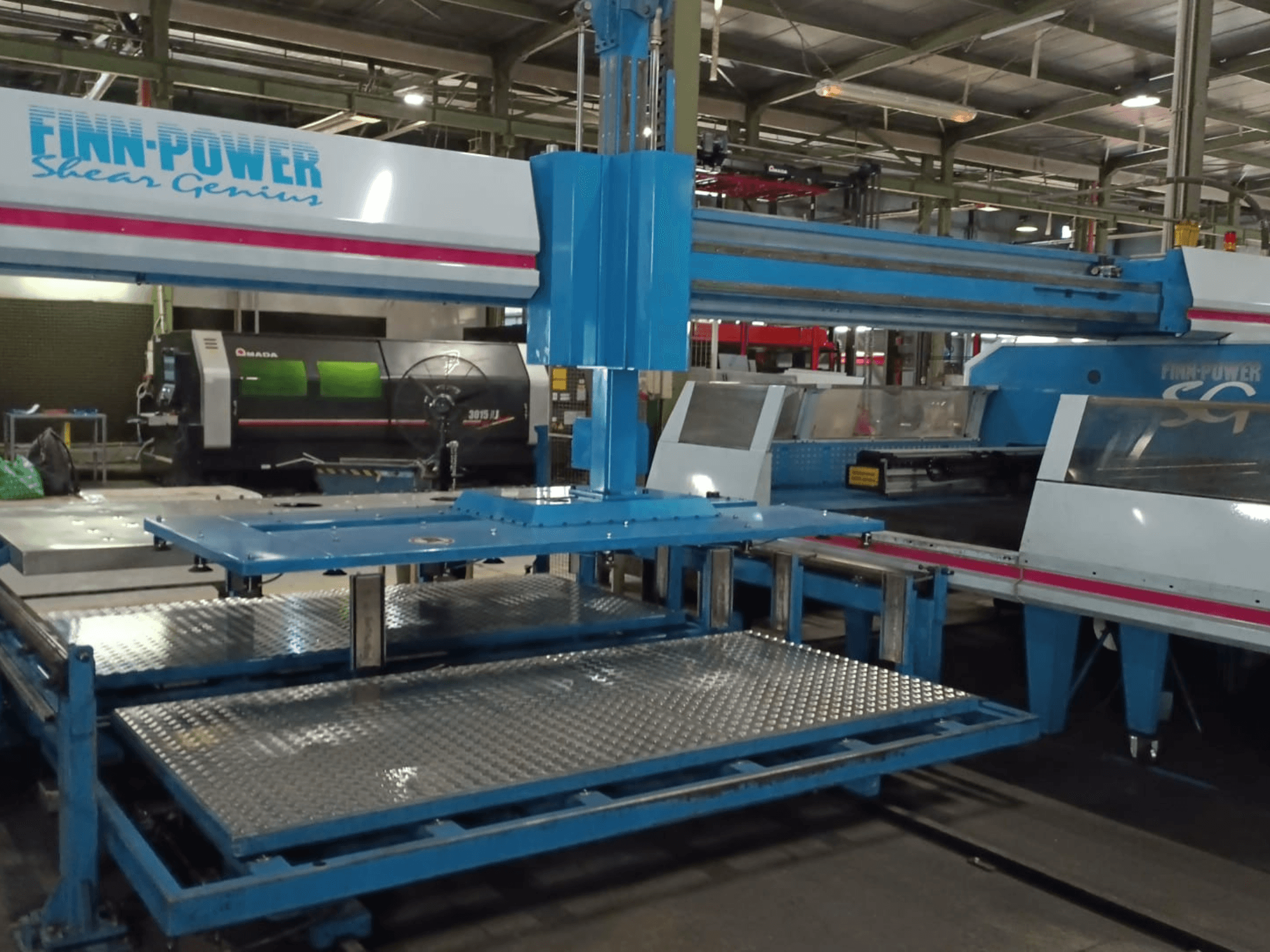 Die CNC-Stanzmaschine „Shear Genius“ vom Typ Finn-Power SG6 in der Vorderansicht, mit Metalltischen und konstruktiven Merkmalen.