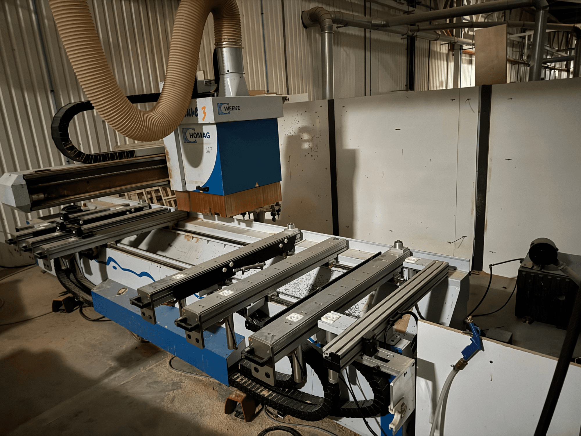 HOMAG CNC-Maschine in blau-weißem Design, Seitenansicht, mit Gleitschienen, Absaugung und montierten Werkzeugen.