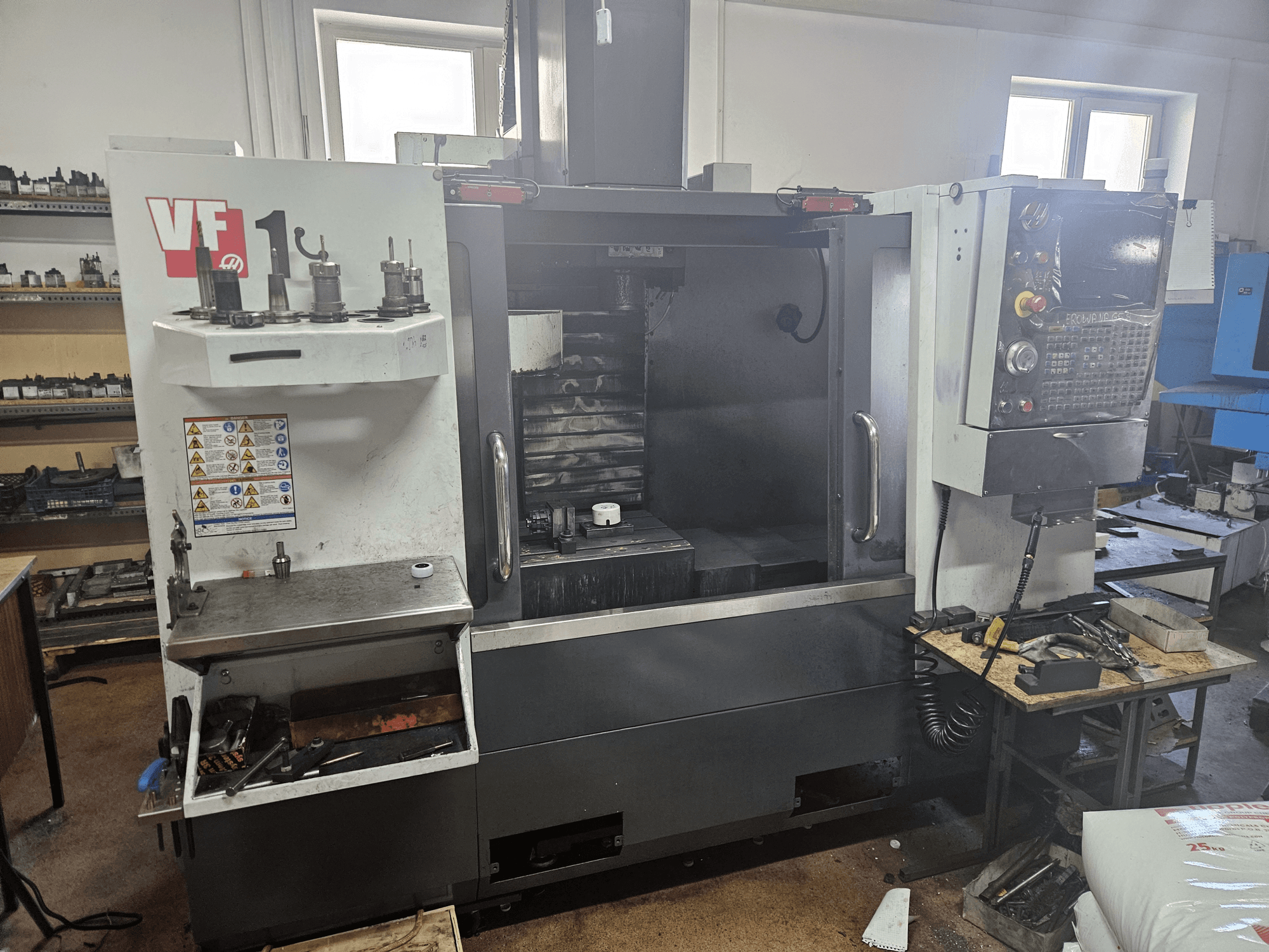 HAAS VF-1 Vertikal-Bearbeitungszentrum, Vorderansicht mit Werkzeugen an der Seite, Bedienfeld sichtbar und Arbeitsbereich im Hintergrund.
