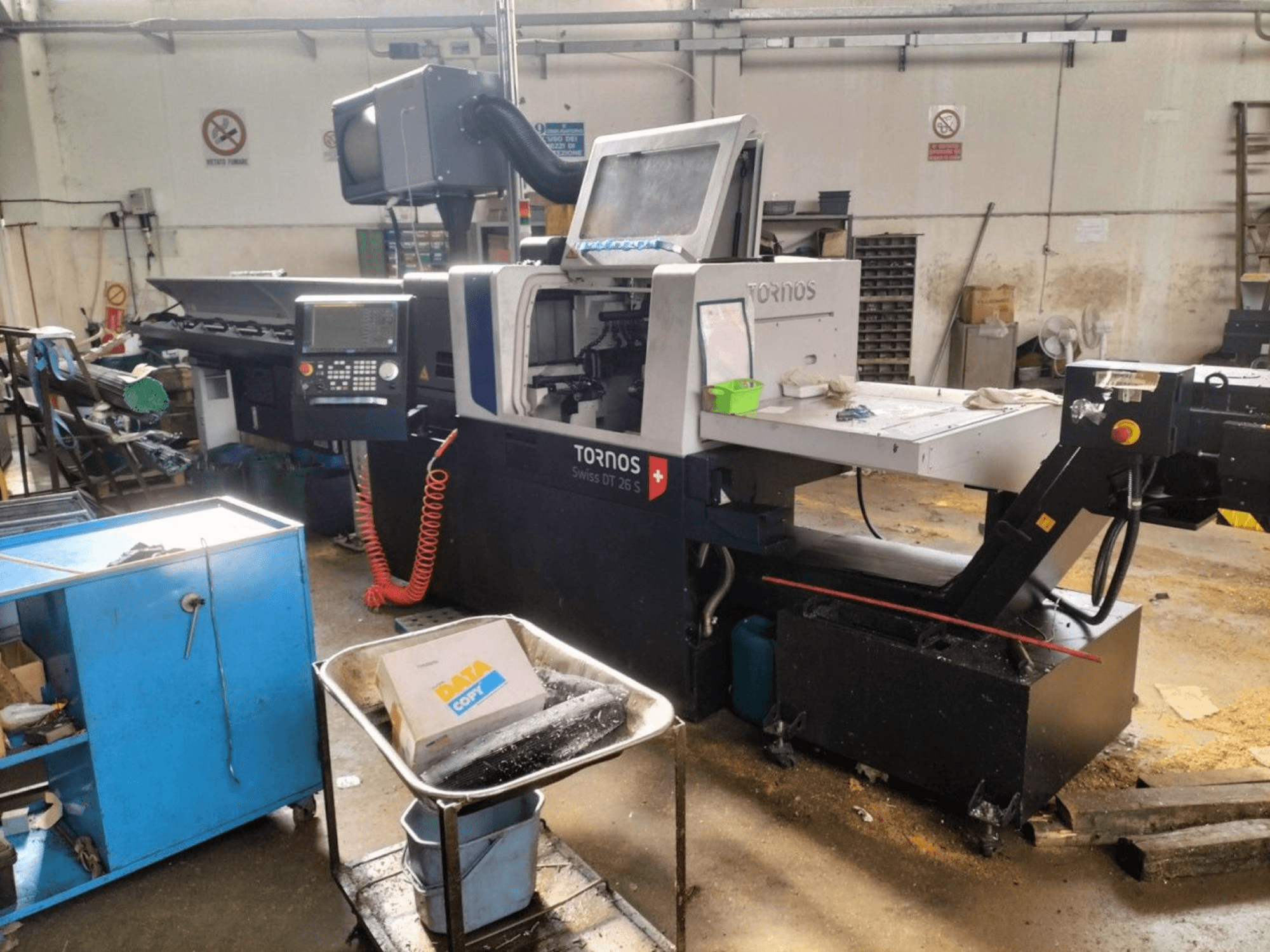 TORNOS Swiss DT 26 S – Drehmaschine vom Typ „Swiss“, Vorderansicht, mit Blick auf das Bedienfeld, den Arbeitsbereich und die umgebende Industrieumgebung.