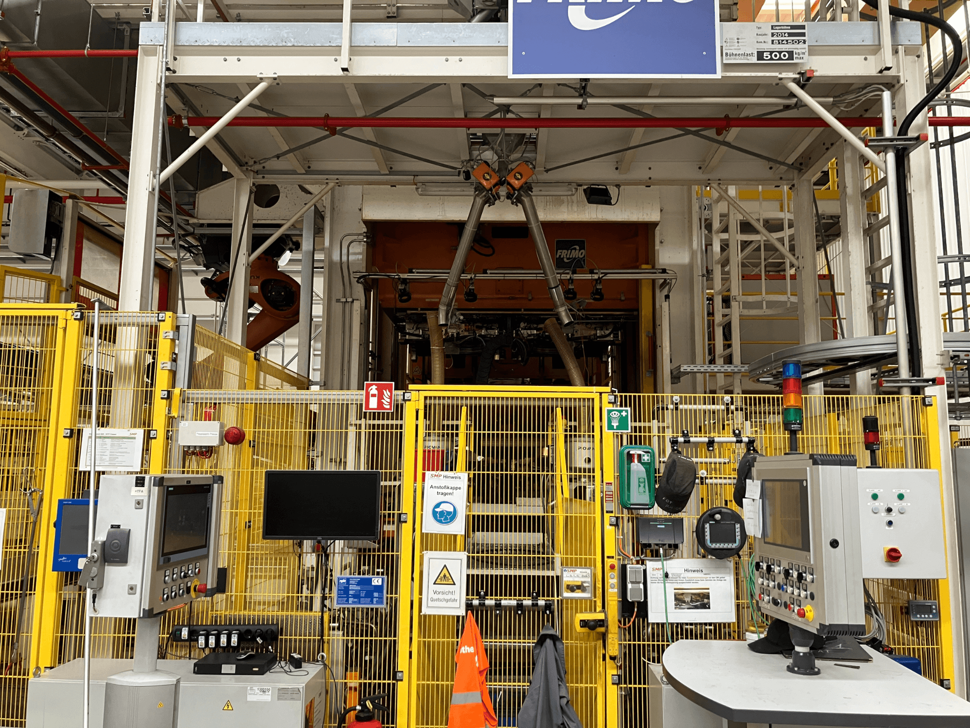 Frontansicht der FRIMO NFPP Thermoformanlage mit Schalttafeln und Sicherheitszäunen in einer gut beleuchteten Industrieumgebung.
