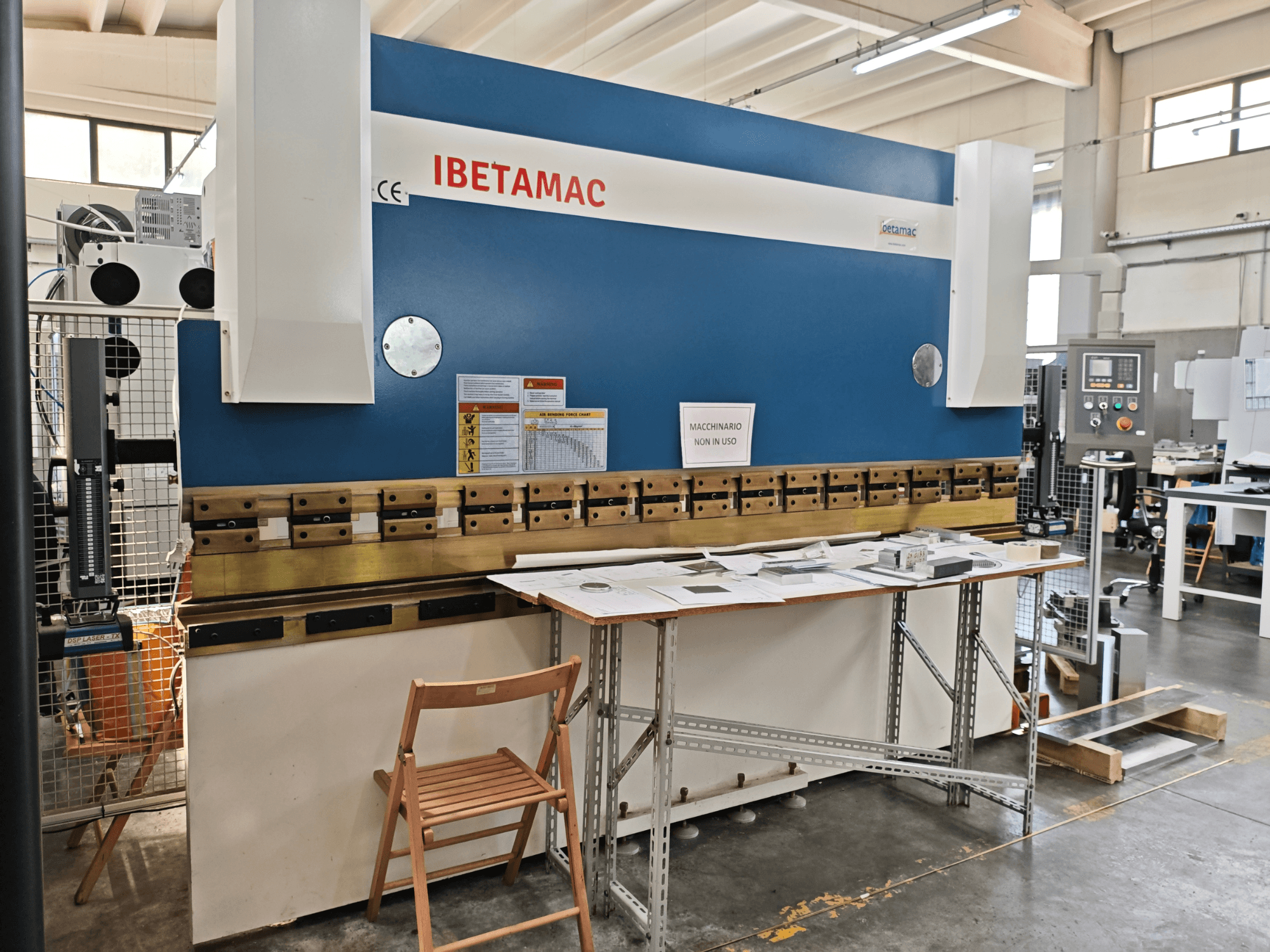 IBETAMAC 3200 100T Abkantpresse in einer Werkstatt, Seitenansicht mit Bedienfeld, Arbeitsbereich und Sicherheitshinweisen.