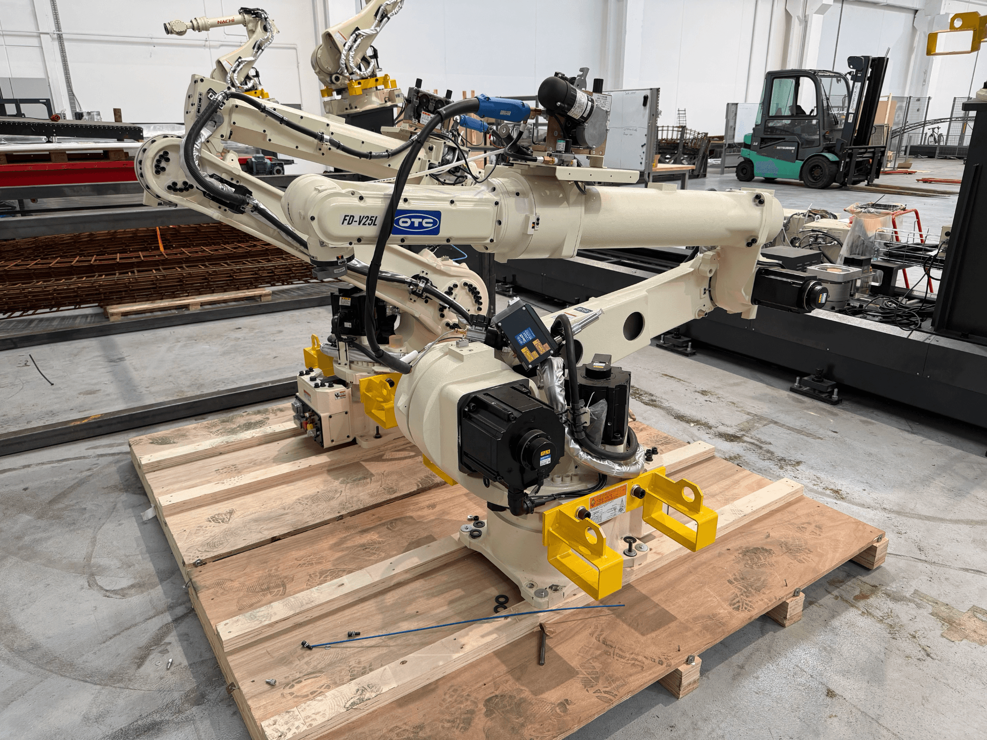 OTC Daihen FD19-V25L-Roboterarm in der Vorderansicht, mit gelben Greifklauen und sichtbaren mechanischen Bauteilen auf einer Holzpalette.
