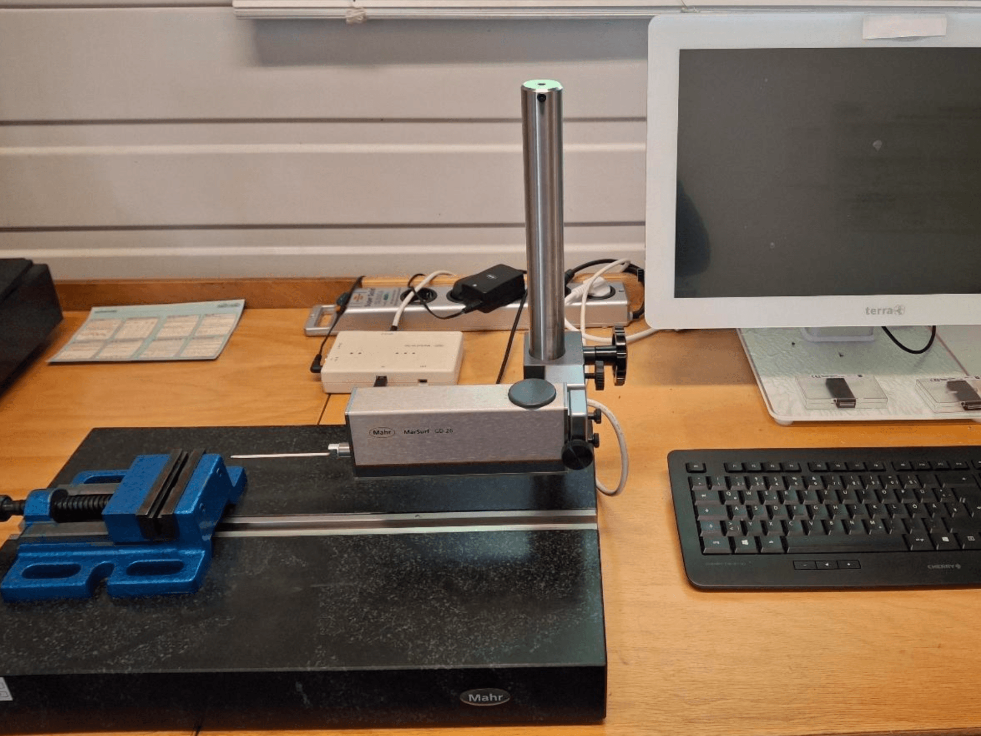 MAHR MARSURF GD 26 KMG auf einer Werkbank mit Messtaster, blauem Schraubstock und Computermonitor. Vorderansicht.
