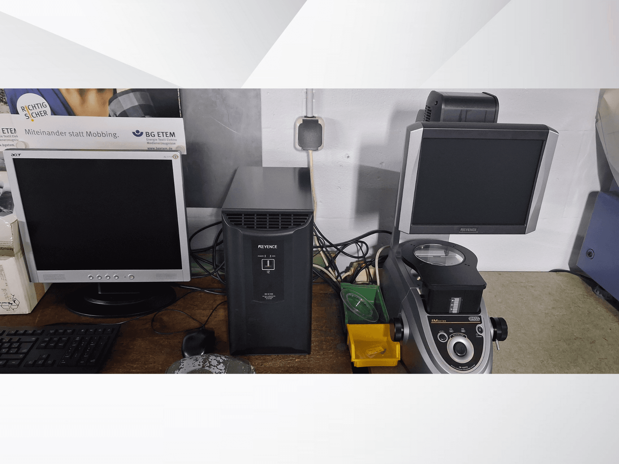 Zwei Computerbildschirme, einer von Acer und einer von Keyence, neben einem schwarzen Gerät und einem Mikroskop, von vorne gesehen.