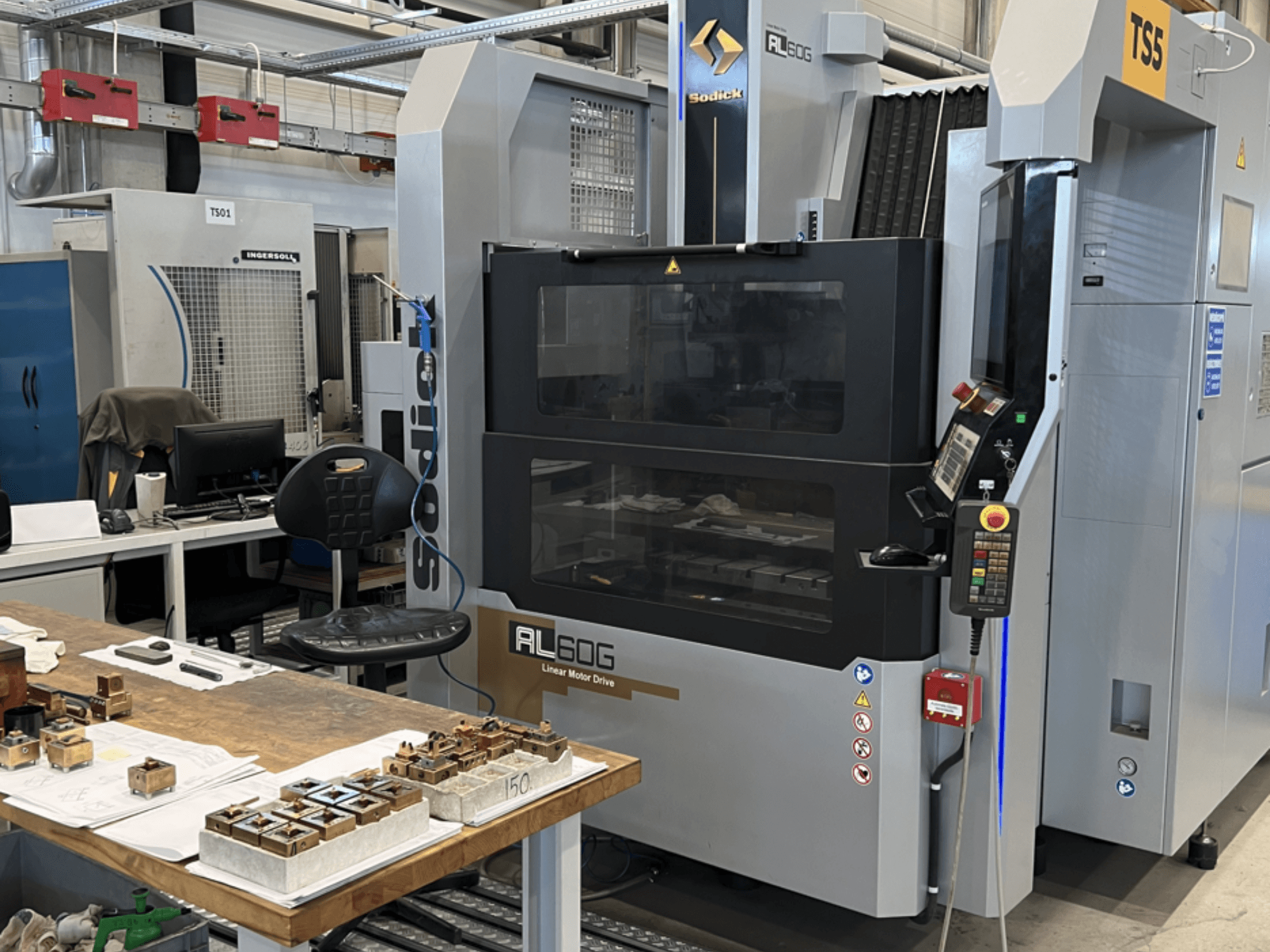Sodick AL60G Senkerodiermaschine; Vorderansicht mit Bedienelementen, Fenster und Arbeitsbereich mit verschiedenen Metallteilen.