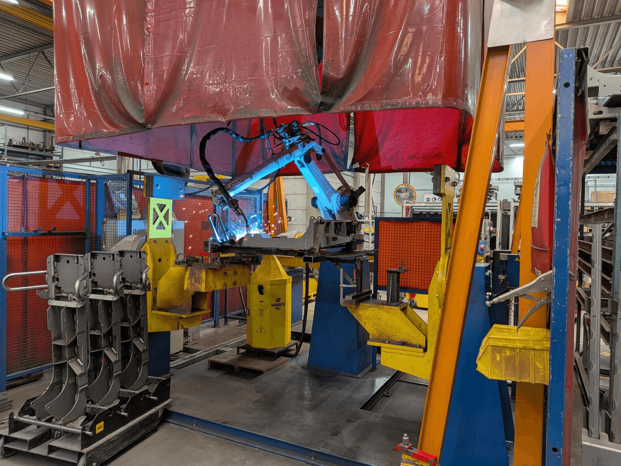 Der Schweißroboter OTC Daihen DR4200 im Einsatz, von vorne gesehen, mit hellblauem Schweißlichtbogen und Schutzabdeckung.