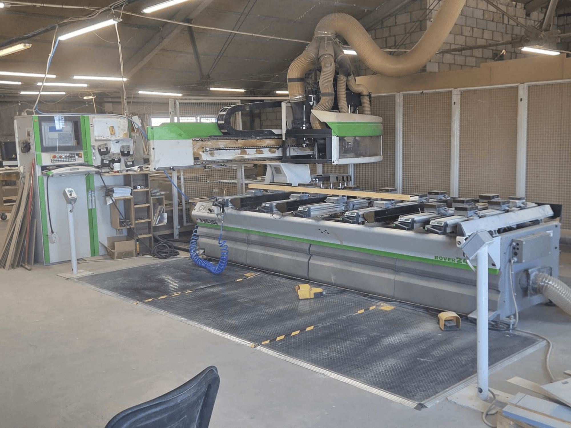 CNC-Bearbeitungszentrum BIESSE Rover 24S in einer Werkstatt, ausgestattet mit einem Bedienpult und einer großen Arbeitsfläche mit Holzteilen.