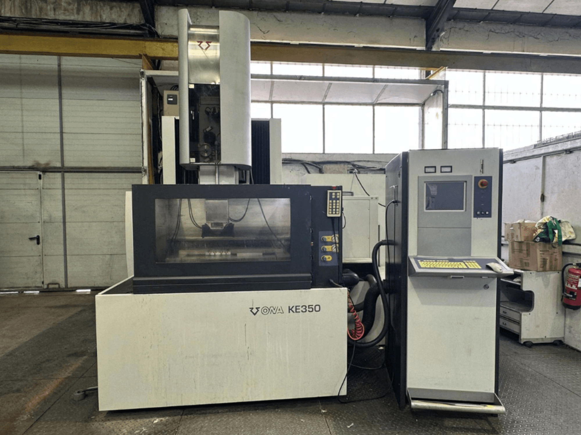 Frontansicht der CNC-Maschine ONA KE350 mit Bedienfeld, Bildschirm und verschiedenen Tasten in einer Industrieumgebung.