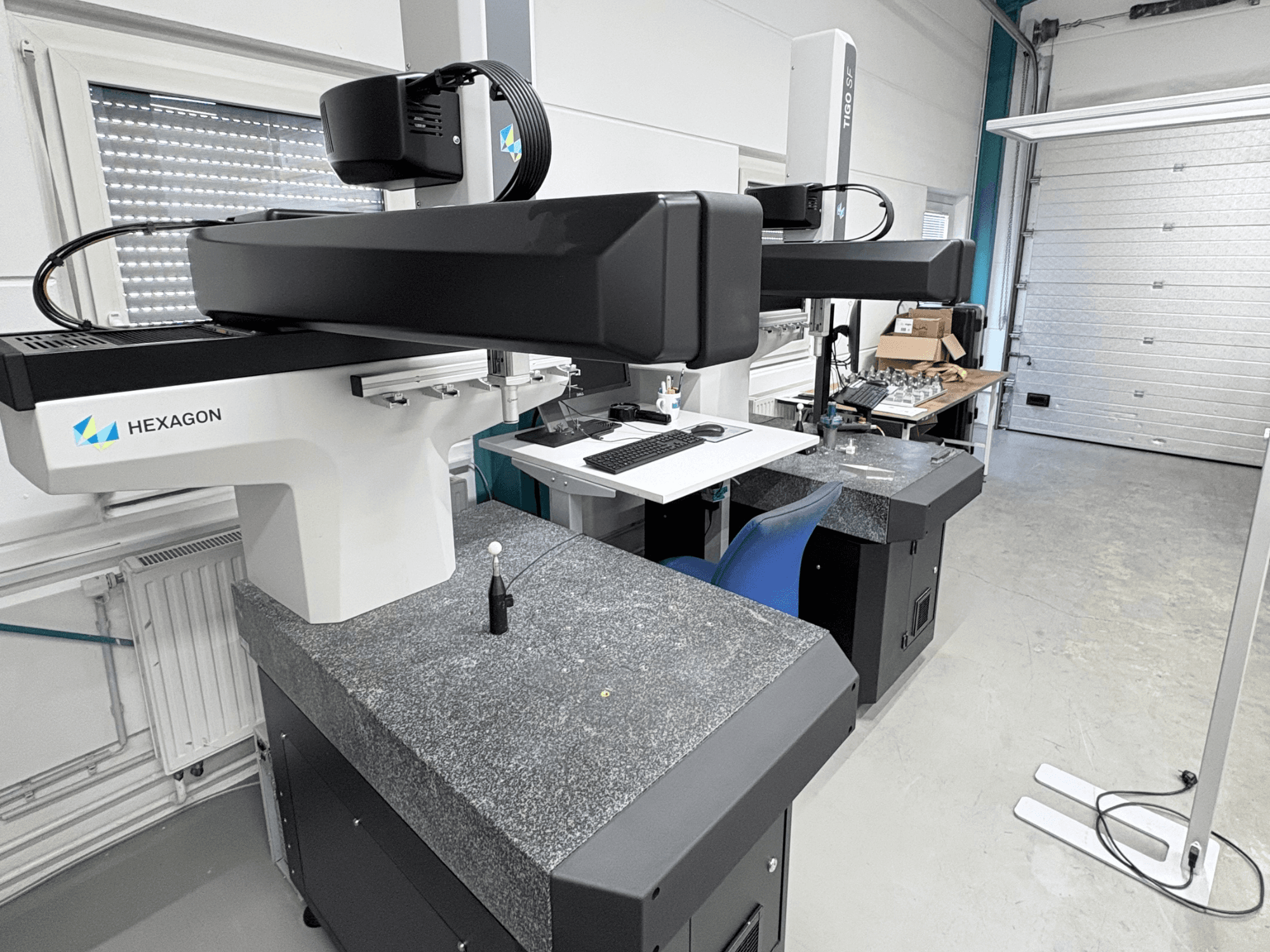 Hexagon Tigo SF-Koordinatenmessgerät in der Werkstatt, ausgestattet mit einem Granitsockel, einem Messkopf und einem nahegelegenen Arbeitsplatz mit Werkzeugen.