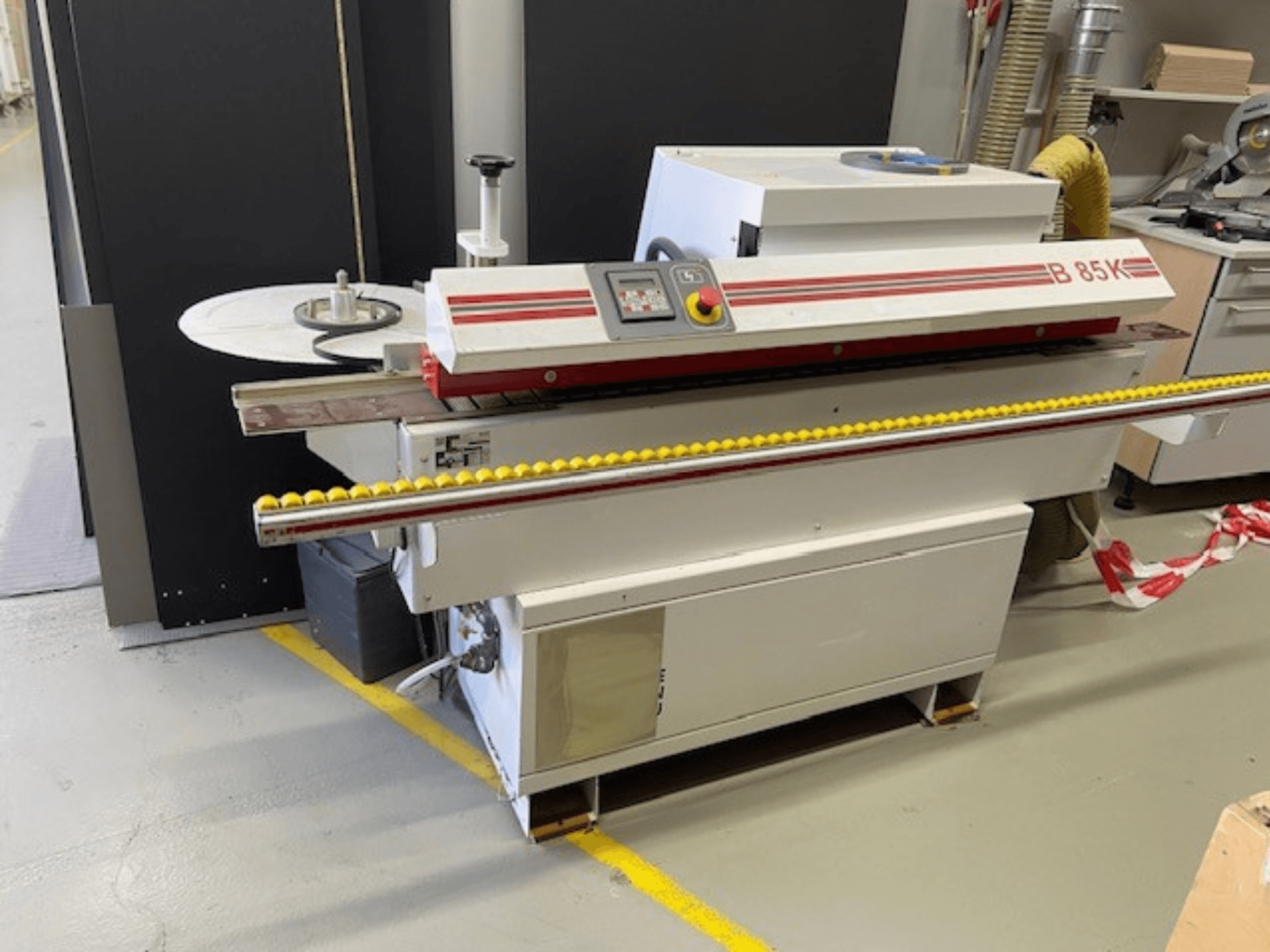 Kantenanleimmaschine B 85K in Weiß und Rot, Vorderansicht, mit Bedienfeld und gelber Rolle für den Materialvorschub.
