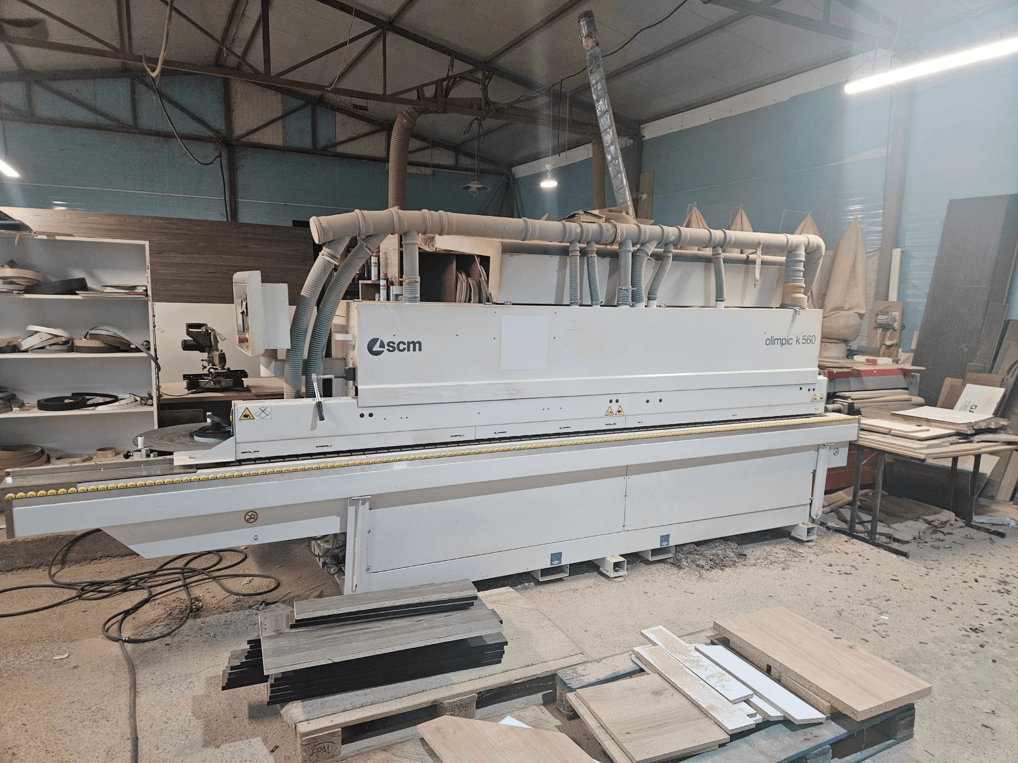 SCM Olimpic K560 Kantenanleimmaschine in einer Werkstatt, Vorderansicht, mit Holzplatten und Werkzeugen auf dem Boden.