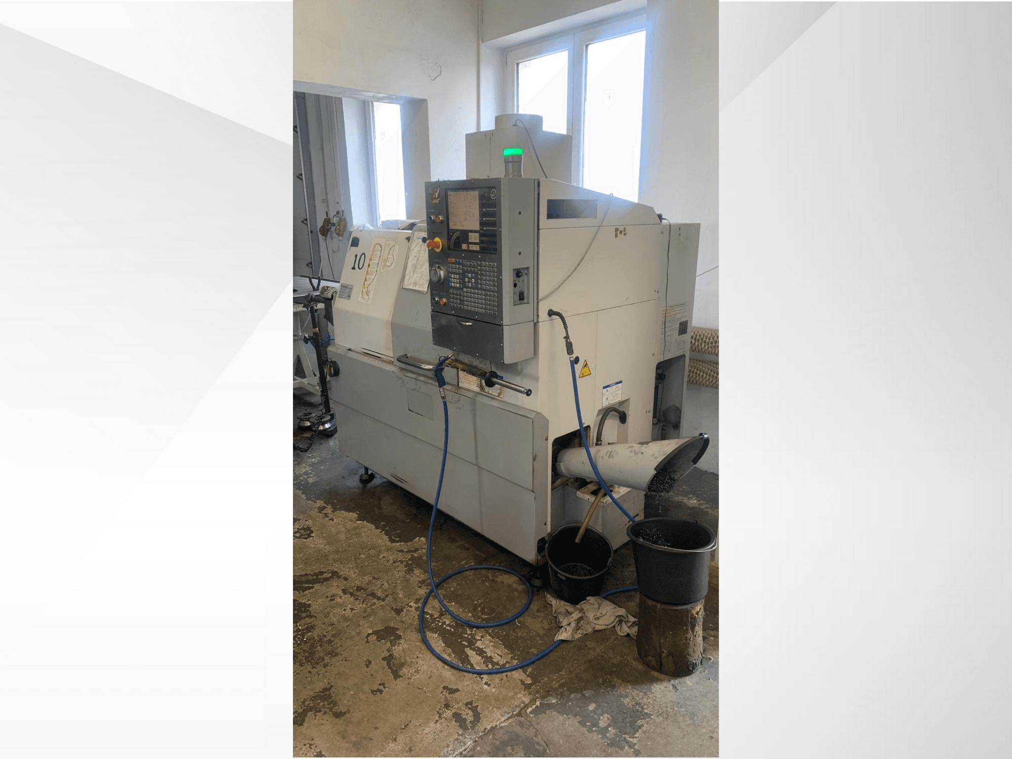 Haas CNC-Maschinenmodell mit Bedienfeld, Seitenansicht, mit Kühlmittelleitung, Abfallrutsche und Lagerbehältern darunter.