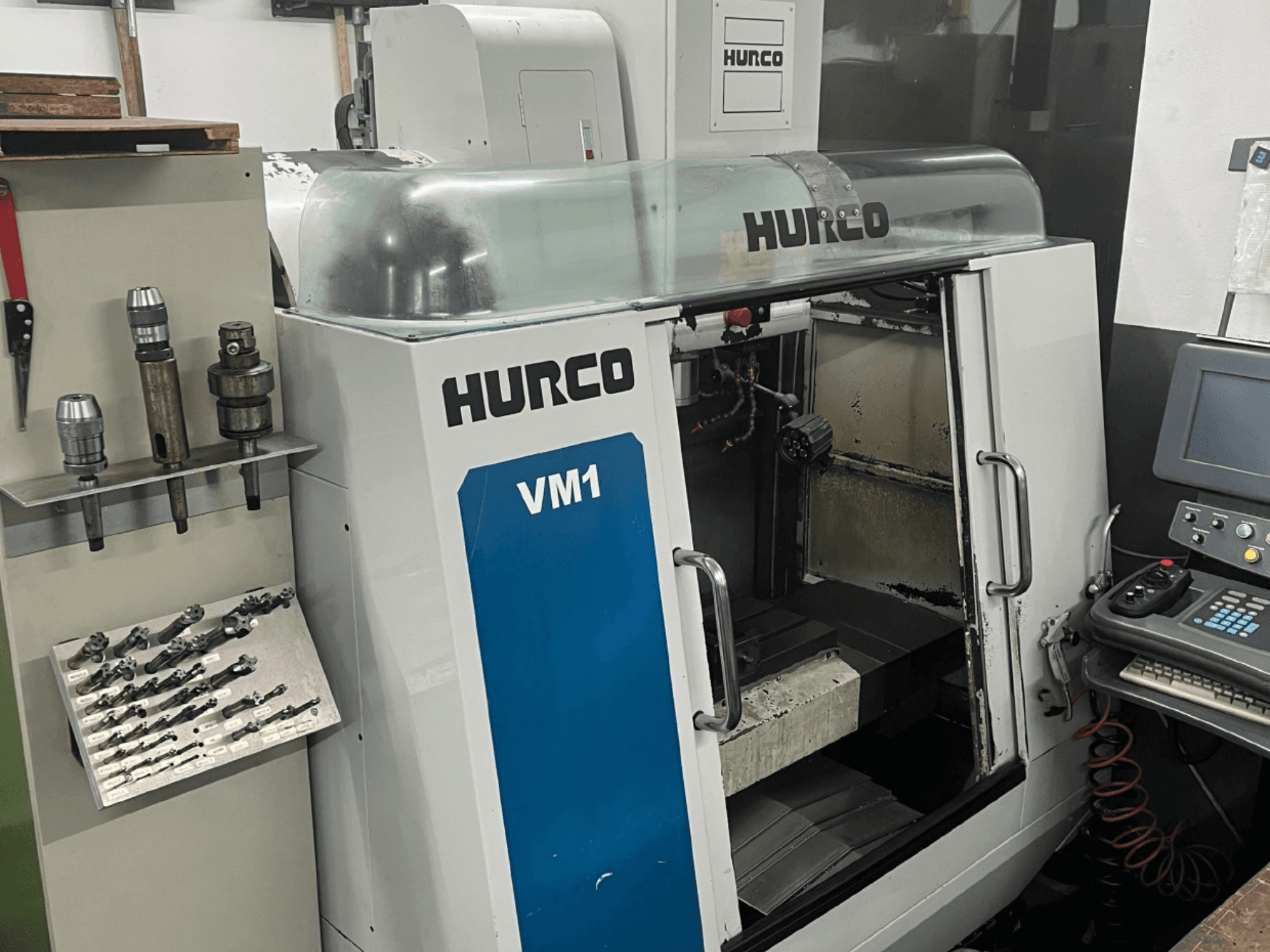 Hurco VM1 Vertikal-Bearbeitungszentrum in der Frontansicht, mit transparenter Abdeckung, Bedienfeld und montierten Werkzeugen.