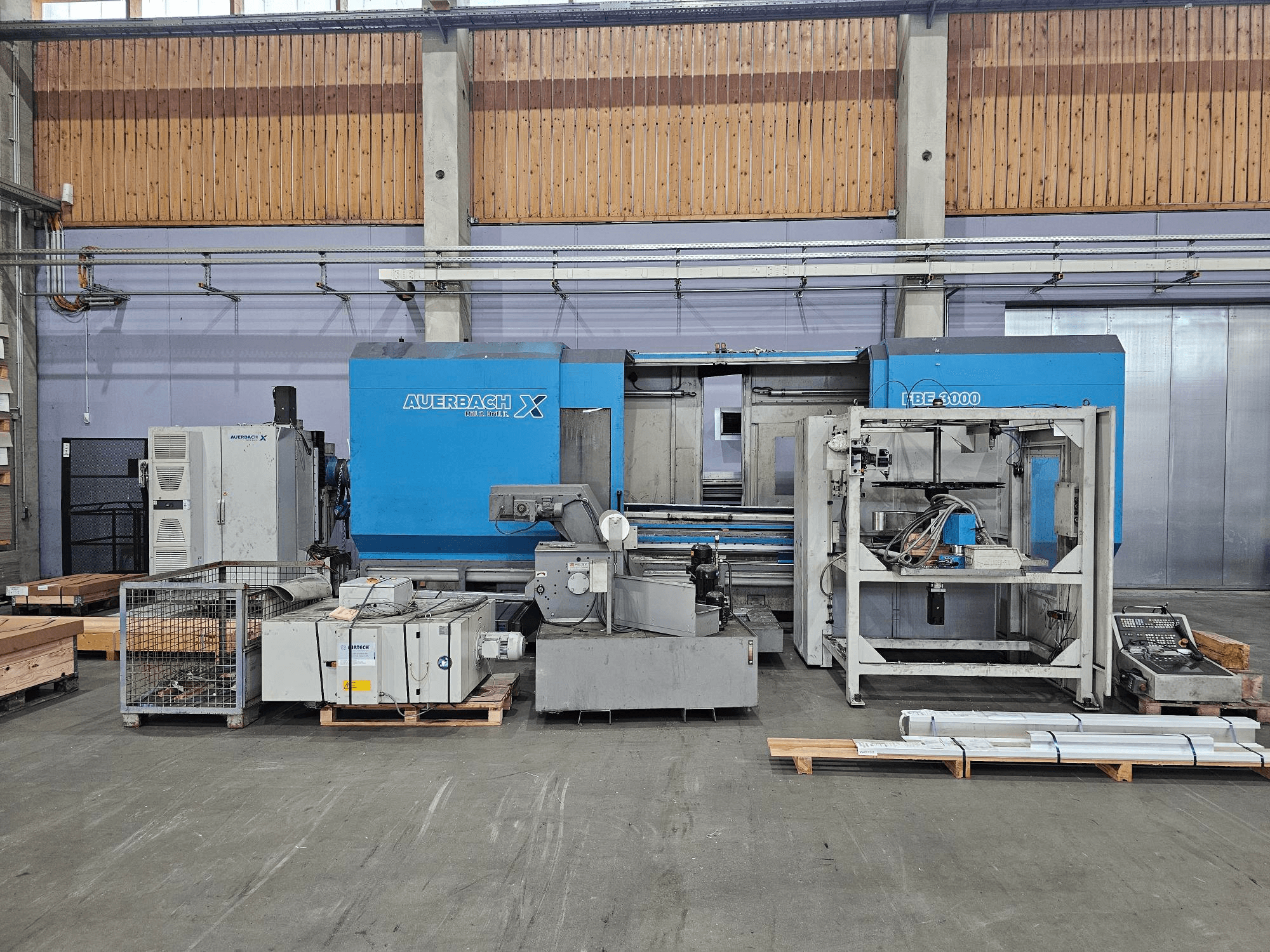Auerbach X LBF-3000 Maschine in einer Werksumgebung, Seitenansicht, mit grauen und blauen Komponenten und sichtbarem Bedienfeld.