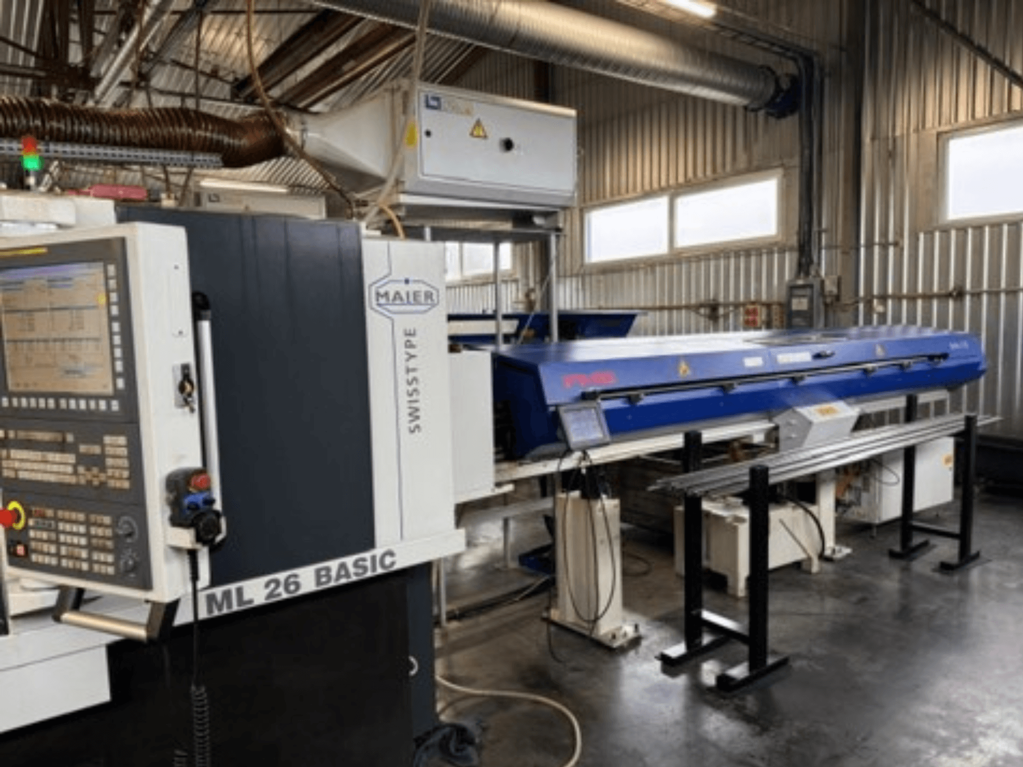 Alternativtext: Vorderansicht einer Drehmaschine vom Typ Maier ML26 C5Y Swiss mit Bedienfeld und angebrachtem blauen Gerät in einer industriellen Umgebung.