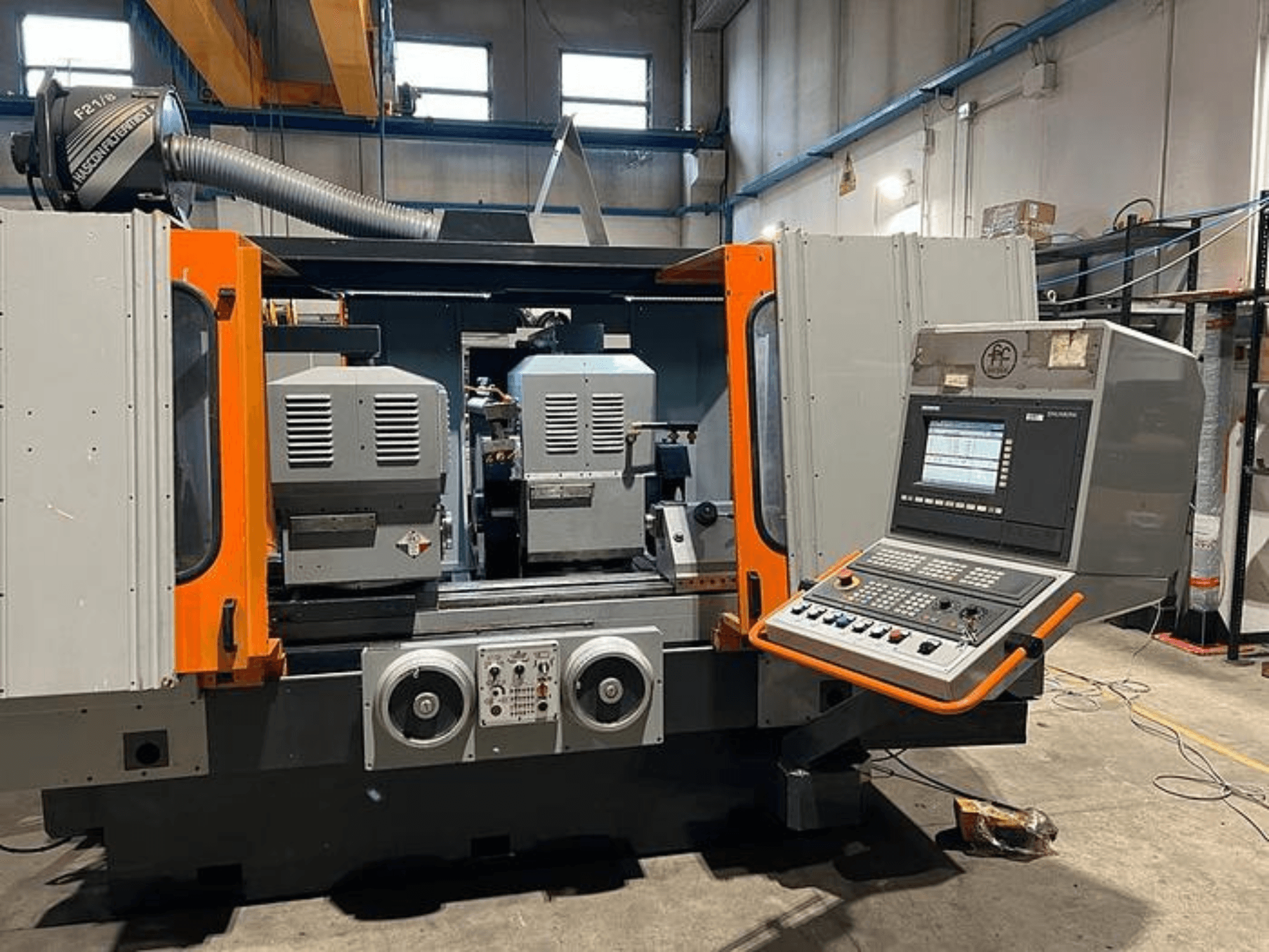 Vorderansicht einer CNC-Maschine mit zwei Spindeln, Bedienfeld und orangefarbenen Akzenten. Mit Lüftungsschacht und Bedienelementen.