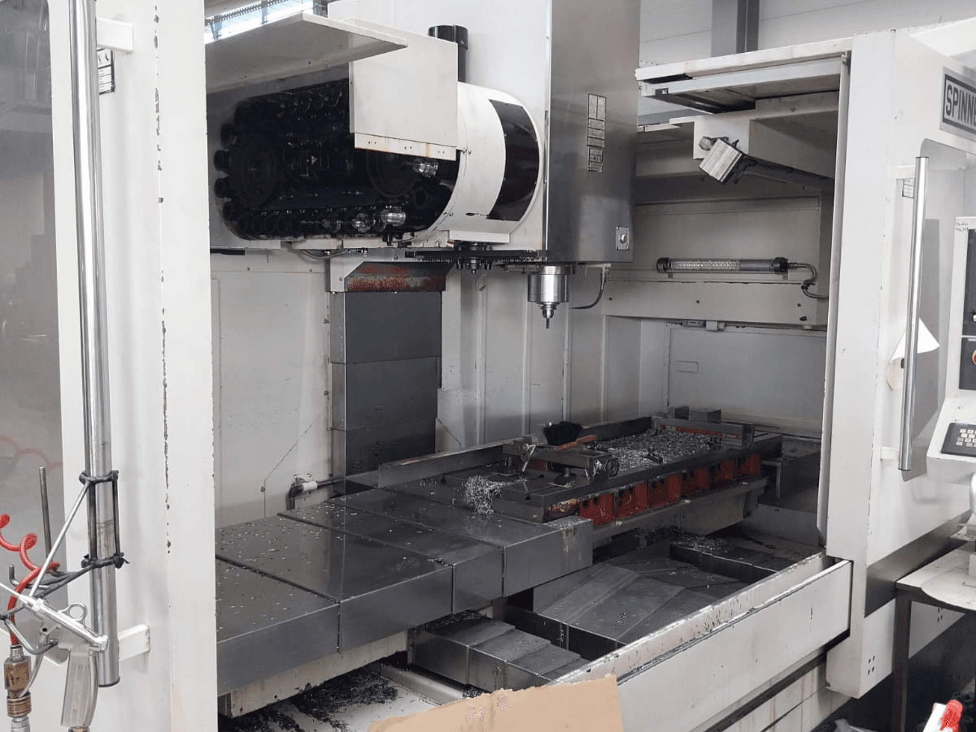 Vorderansicht des vertikalen Bearbeitungszentrums SPINNER MVC 1600 mit offenem Arbeitsraum, Spindel und Metallspänen auf dem Tisch.