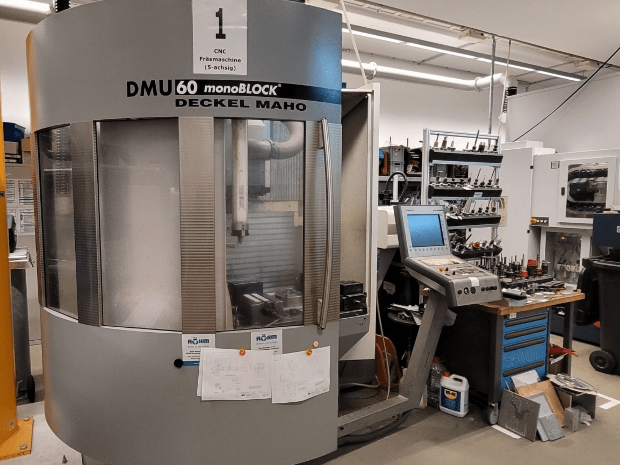 CNC-Fräsmaschine DECKEL MAHO DMU 60 monoBLOCK in der Frontansicht, daneben Bedienpult und Werkzeuglager.