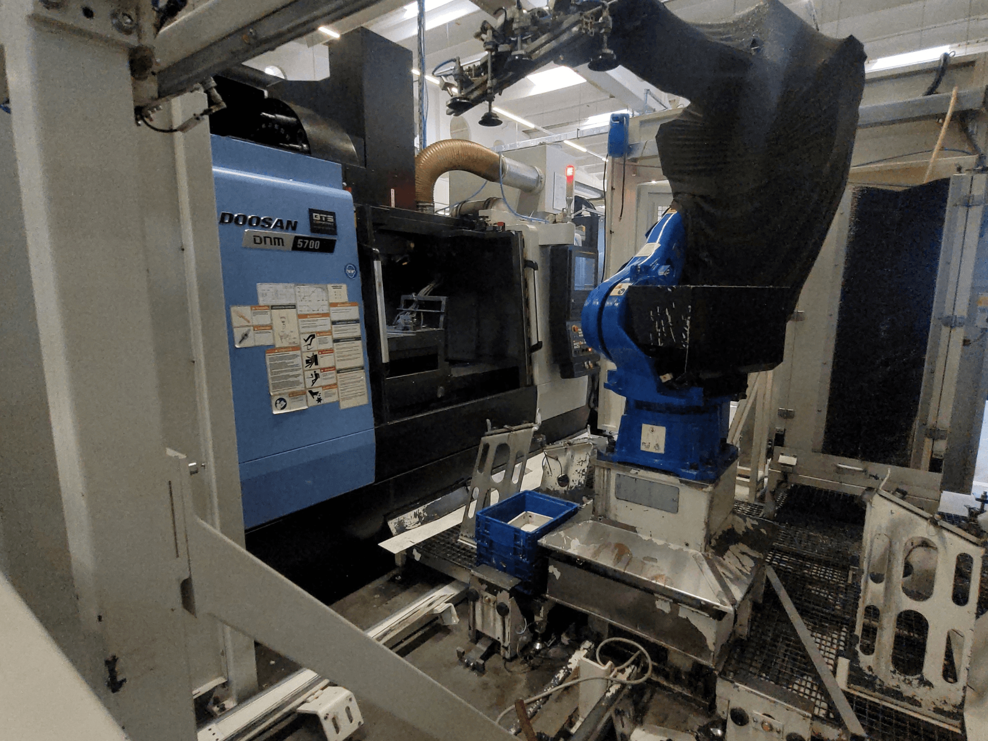 Das vertikale Bearbeitungszentrum DOOSAN DNM 5700 in einer Fabrikumgebung, das seine Vorderansicht und die Integration eines Roboterarms zeigt.
