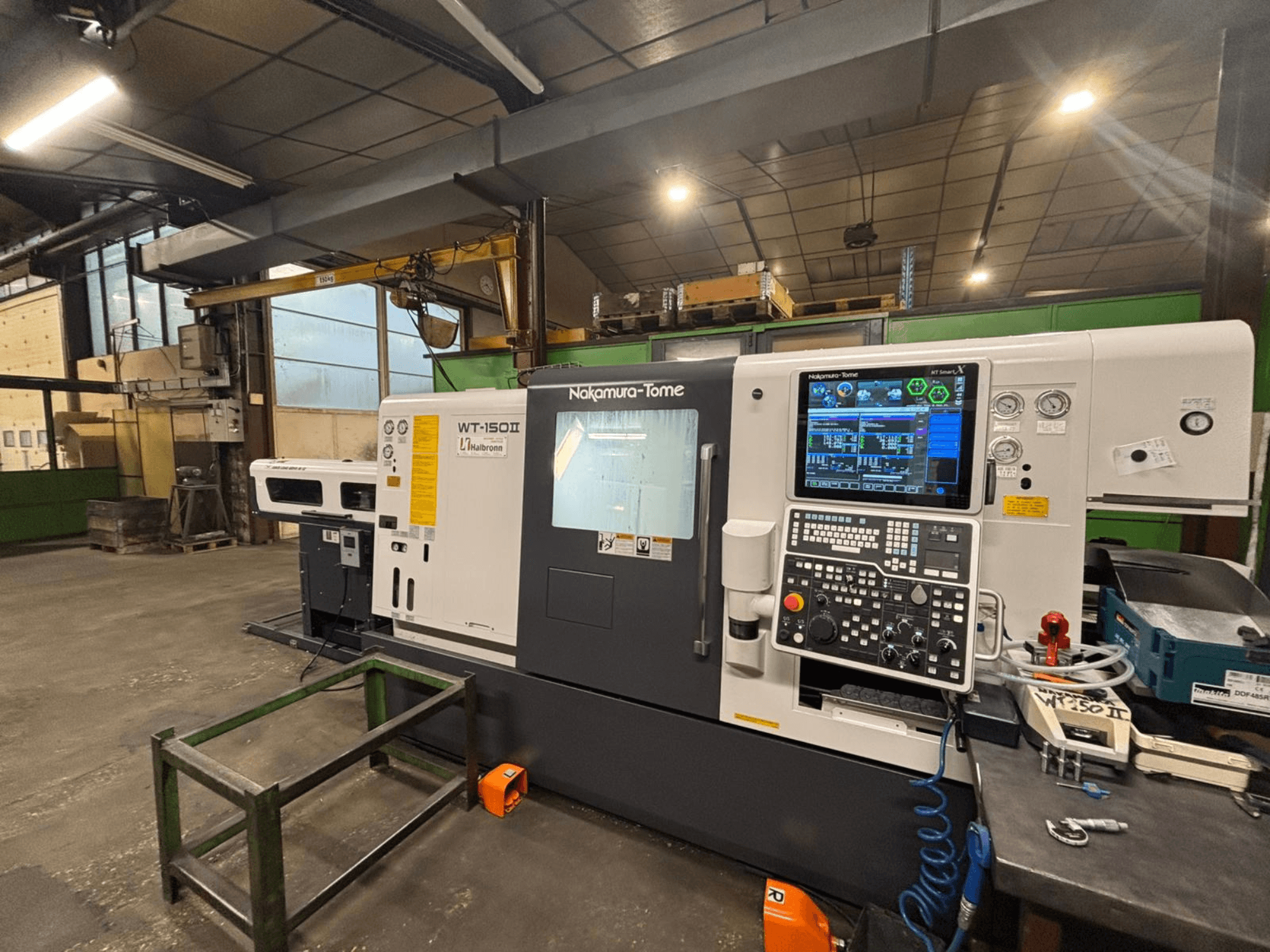 Nakamura-Tome WT-150II Maschine, Vorderansicht, mit Bedienfeld und Werkzeugen auf einer Werkbank in einer Werkstattumgebung.