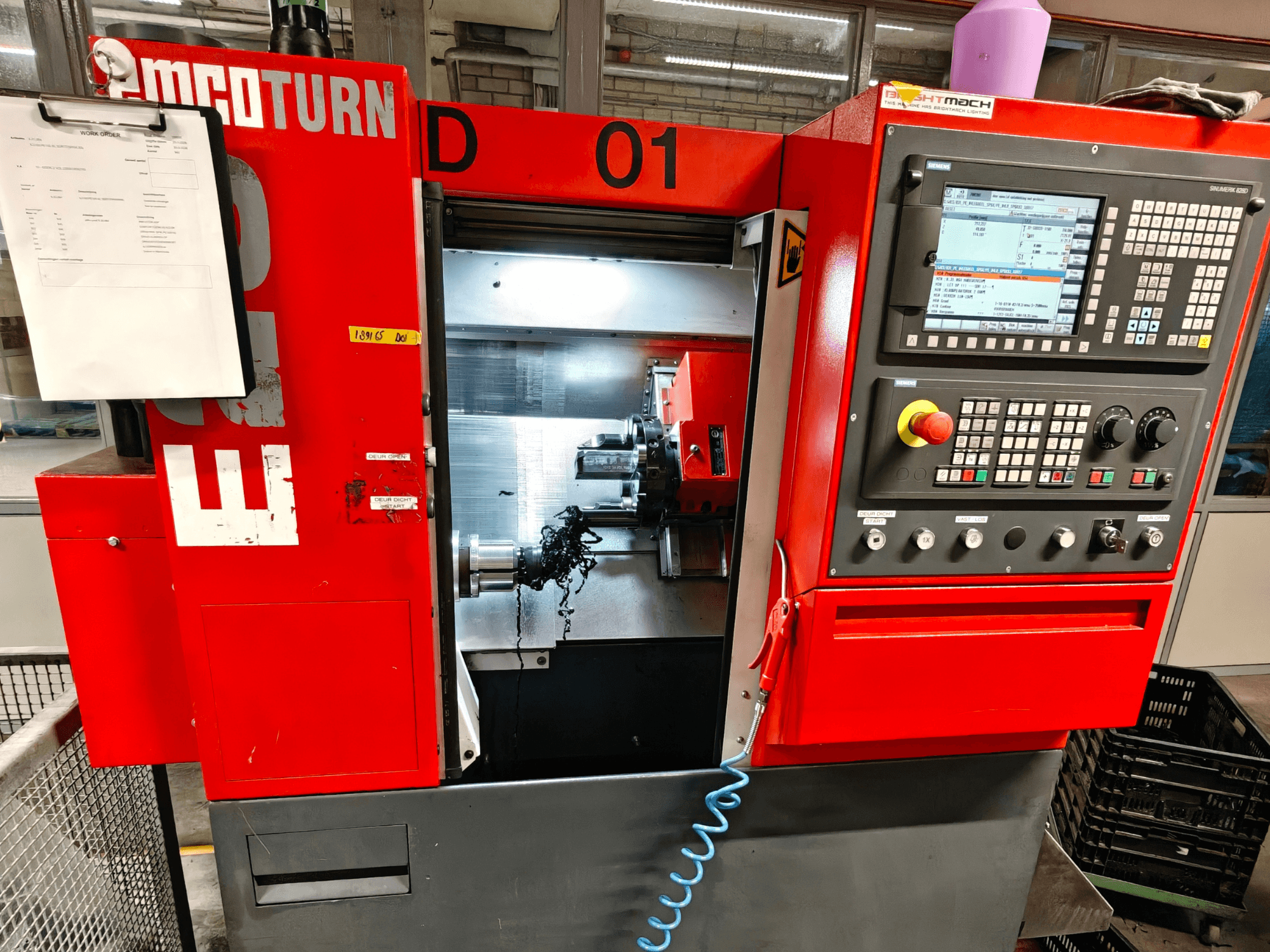 Frontansicht der Horizontaldrehmaschine EMCO TURN E25 mit Bedienelementen, Werkzeughalter und Arbeitsbereich mit Spänen.