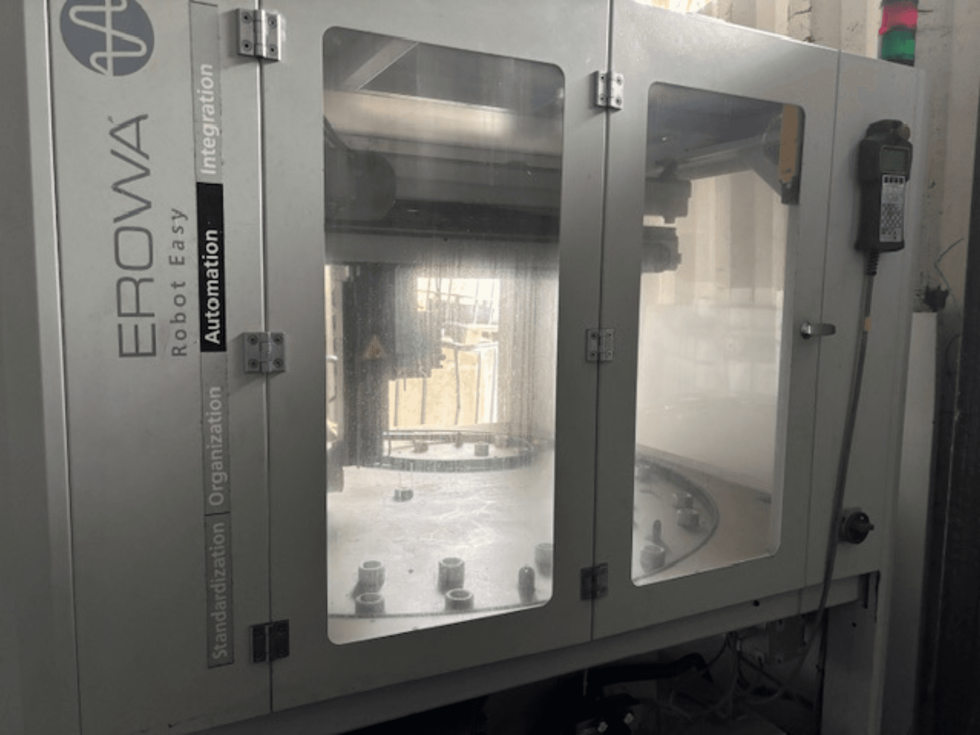 Frontansicht des EROWA Robot Easy Automation; mit durchsichtigen Türen, sichtbaren Automatisierungskomponenten und Bedienfeld.