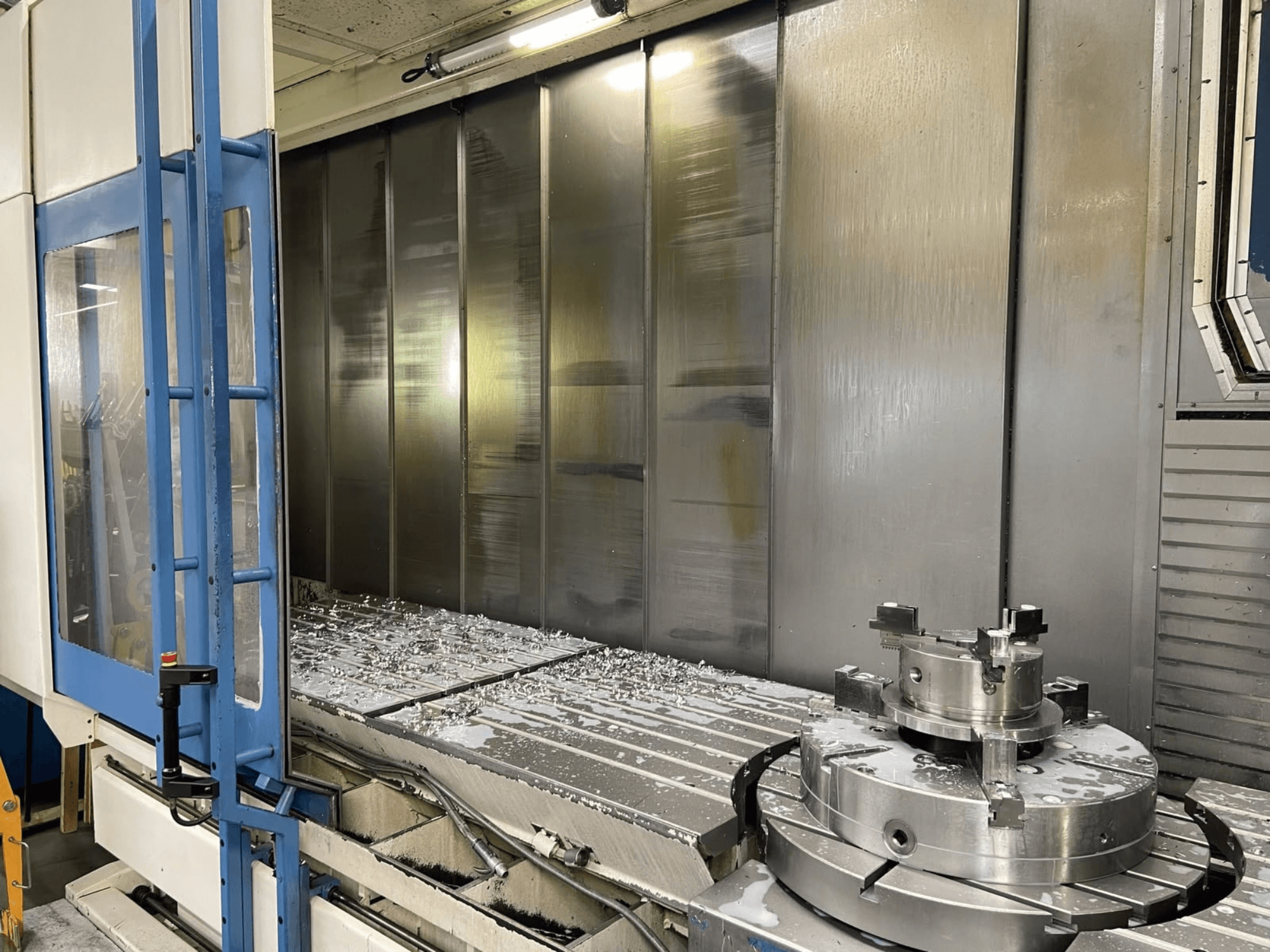 Vertikales Bearbeitungszentrum AXA VHC-3-3000-M/E, Vorderansicht, mit gefrästen Metallspänen auf dem Arbeitstisch und den Schneidwerkzeugen.