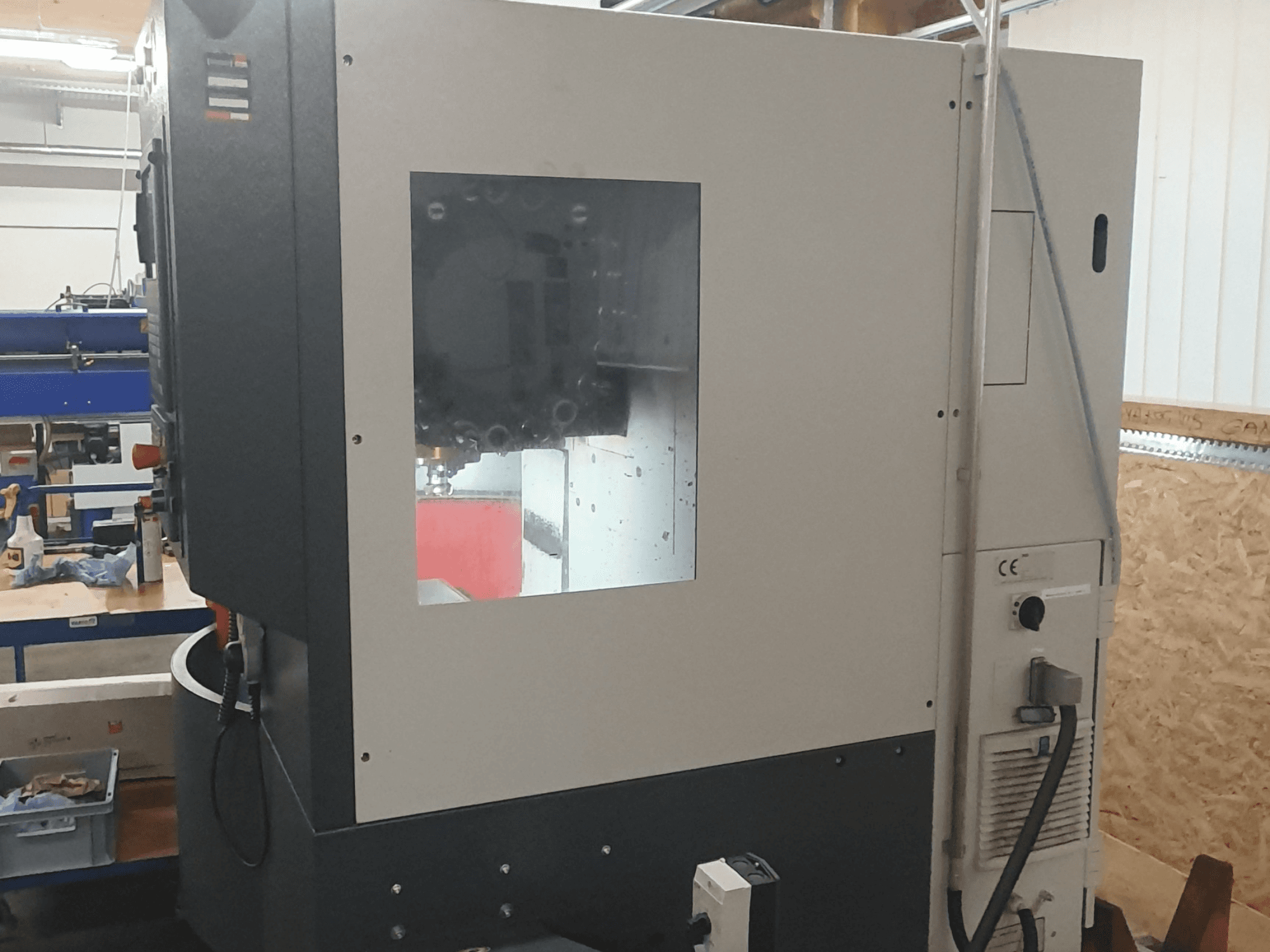 Seitenansicht einer Metallbearbeitungsmaschine mit sichtbarem Bedienfeld, großem Sichtfenster und komplizierten inneren Komponenten.