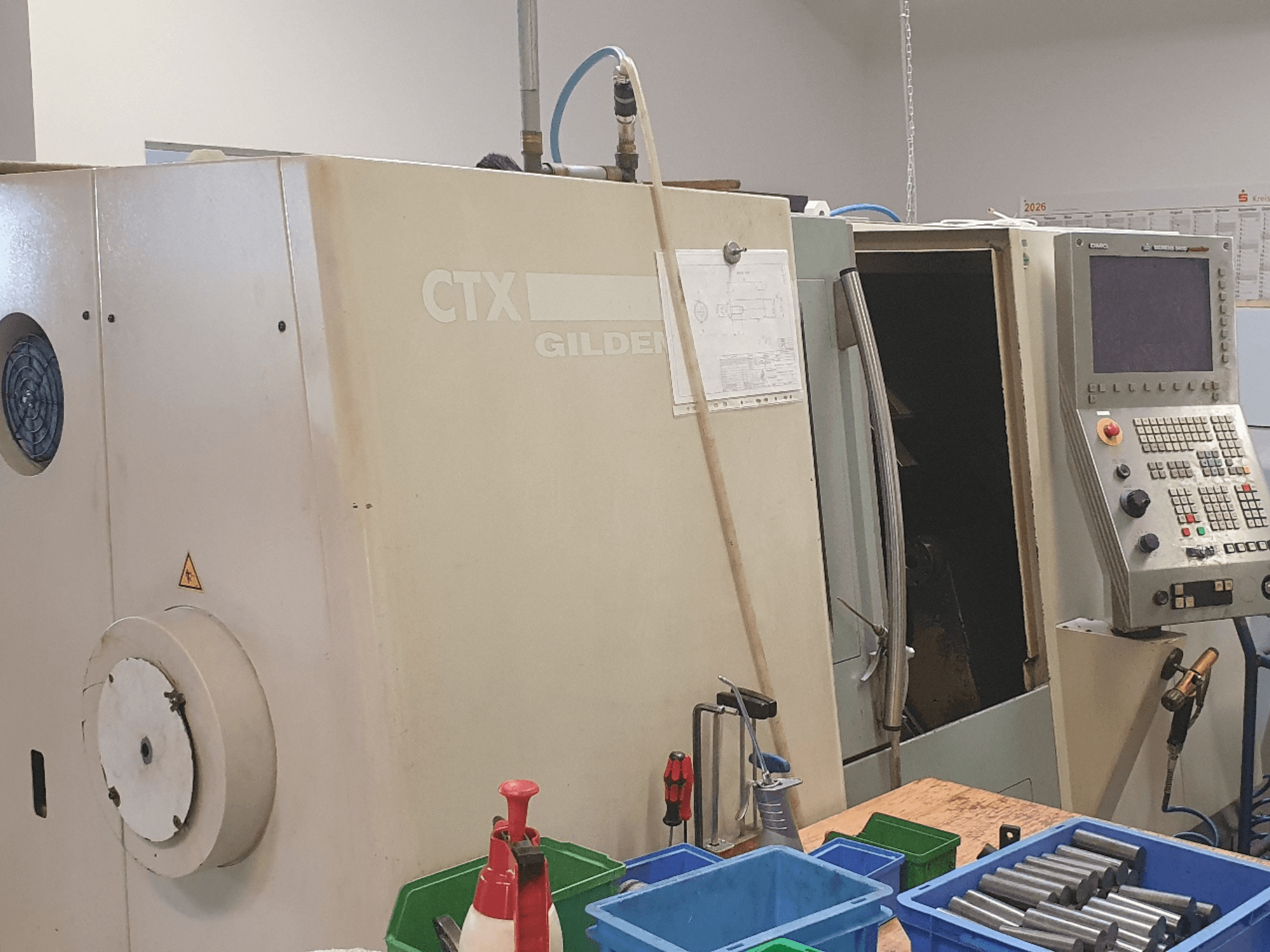 Vorderansicht der Horizontal-Drehmaschine DMG GILDEMEISTER CTX 310, Bedienfeld sichtbar, Werkzeuge und Behälter im Vordergrund.