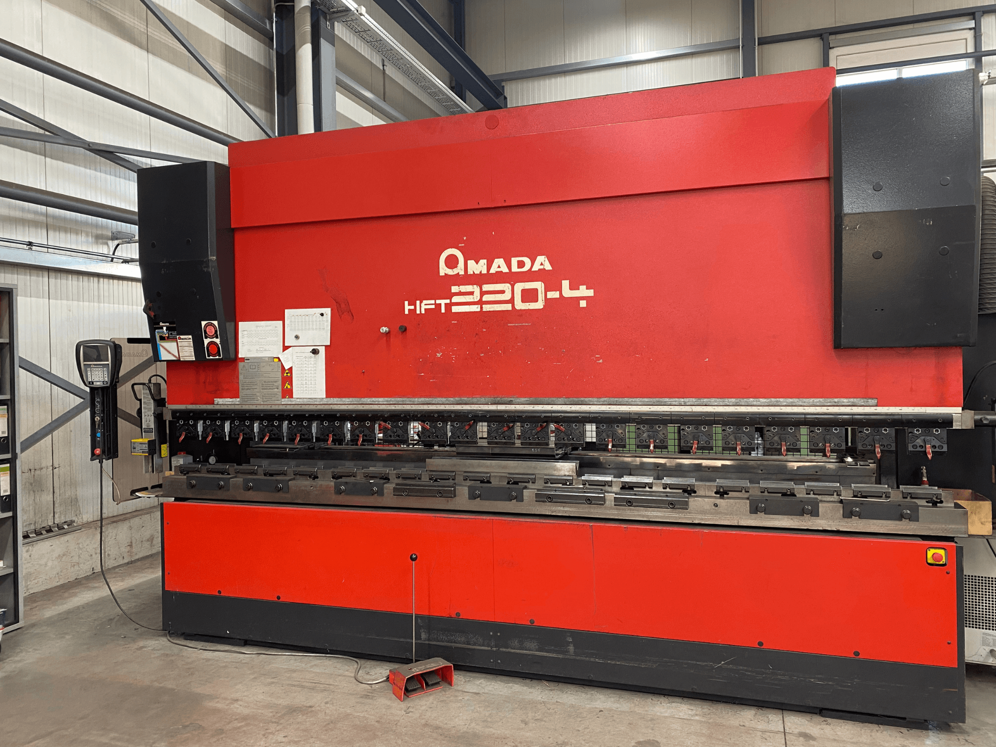 Rote AMADA HFT 220-4 Abkantpresse in einer Werkseinstellung, Vorderansicht mit Bedienfeld und Biegewerkzeugen auf der Arbeitsfläche.