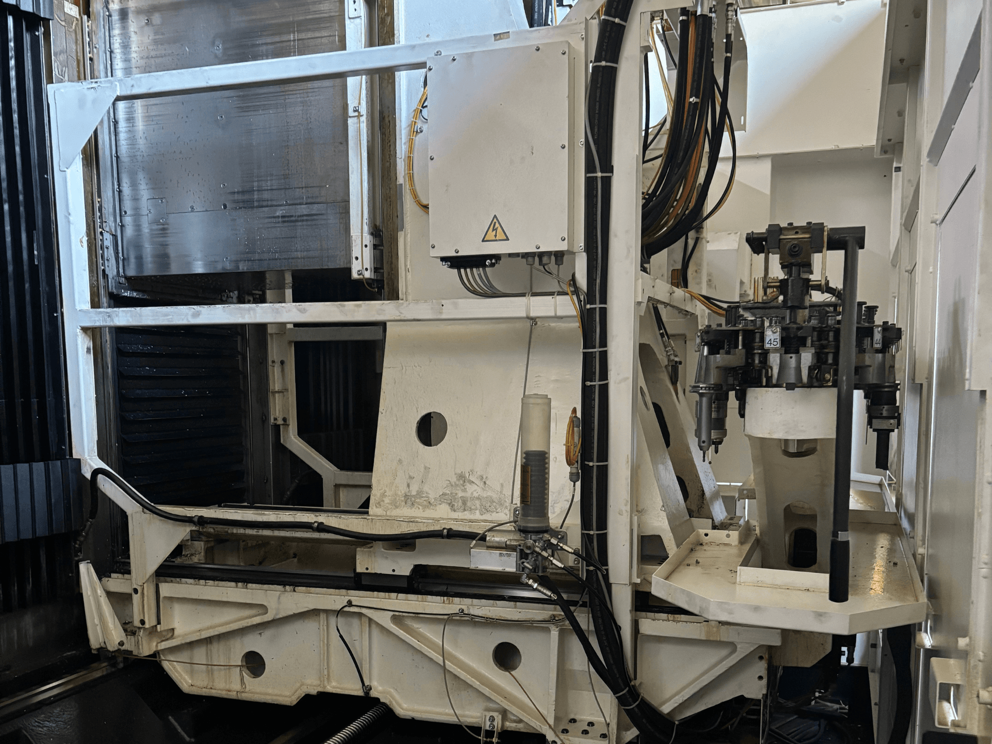 Seitenansicht einer Industriemaschine, die eine weiße CNC-Fräsmaschine mit sichtbaren Werkzeugen, Rohren und einem Bedienfeld zeigt.