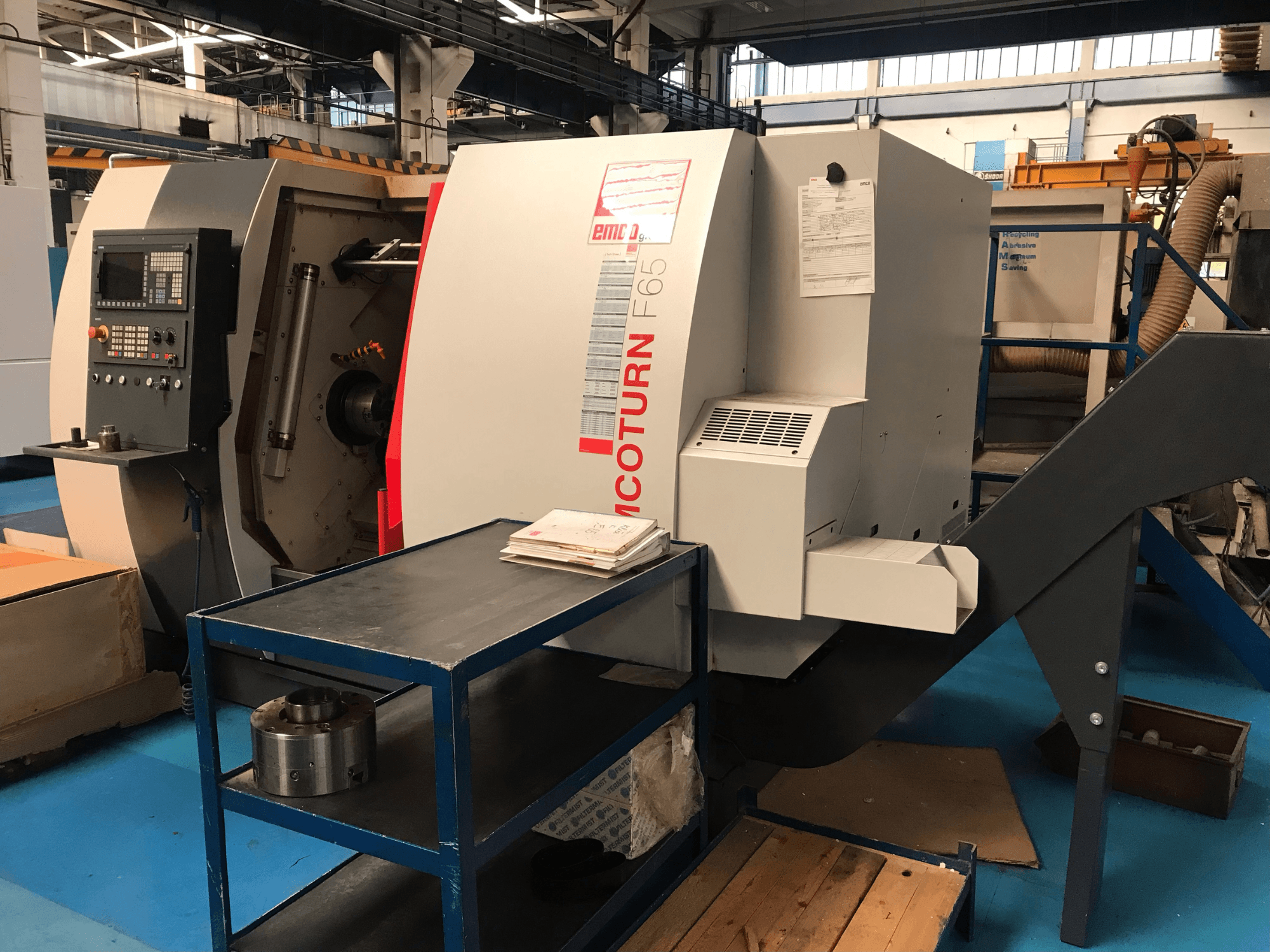 Die horizontale Drehmaschine EMCO Emcoturn 65 in Seitenansicht, mit Blick auf die Bedienelemente und den Arbeitsbereich sowie Metallteile in der Nähe.