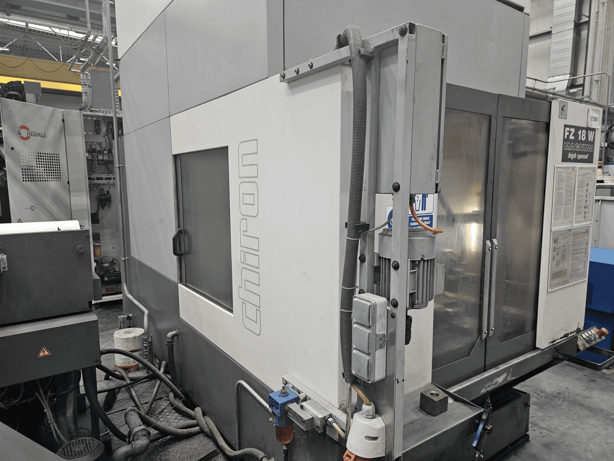 Chiron FZ 18 W Magnum CNC-Maschine, Seitenansicht, mit Bedienfeld, Fenster und sichtbaren hydraulischen Anschlüssen.